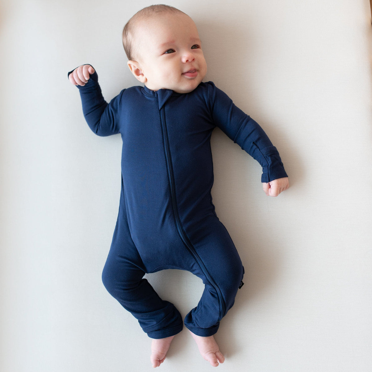 Infant laying on an Oat surface while wearing a Zippered Romper in Navy