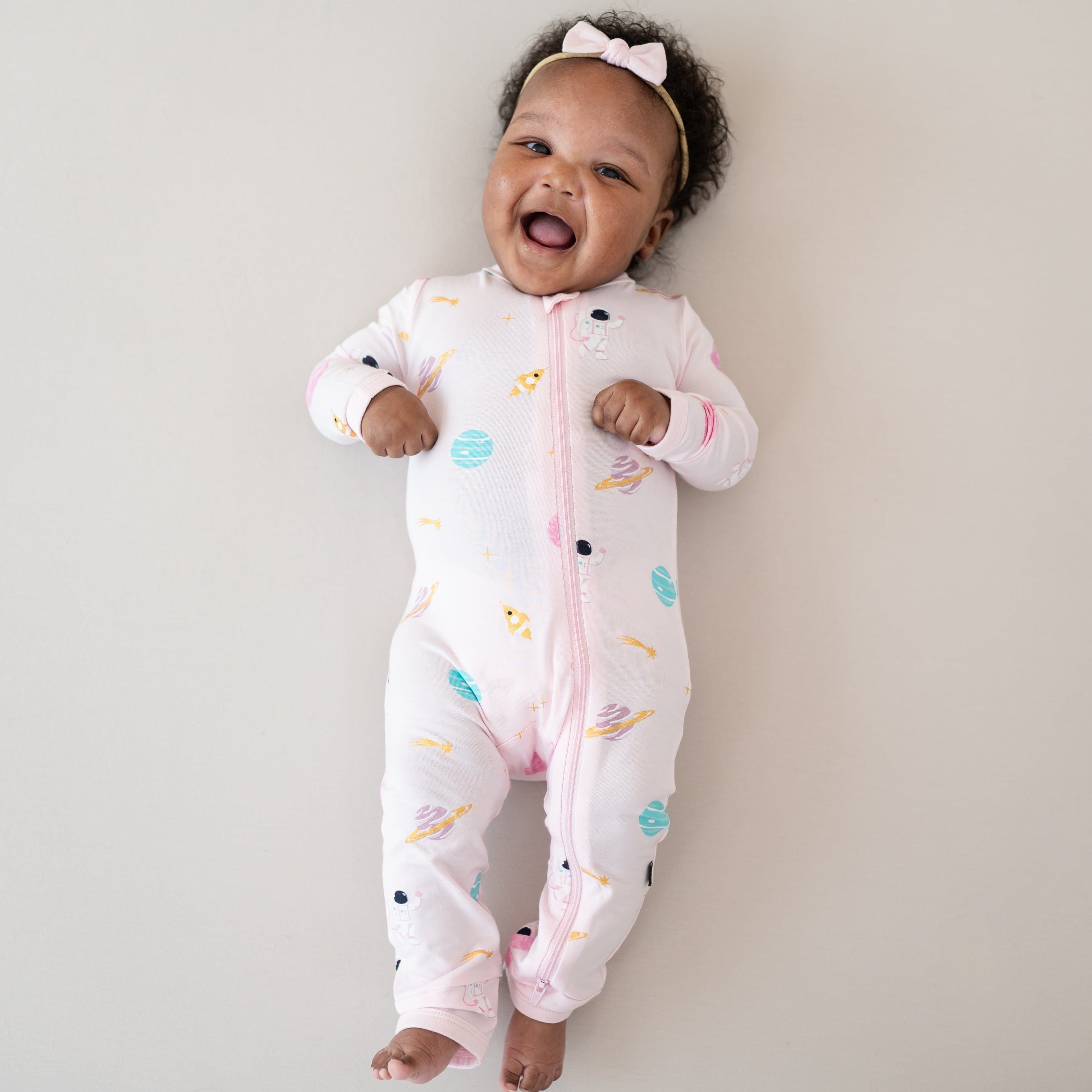 Laughing infant wearing the Zippered Romper in Sakura Space with Tiny Nylon Bow in Sakura