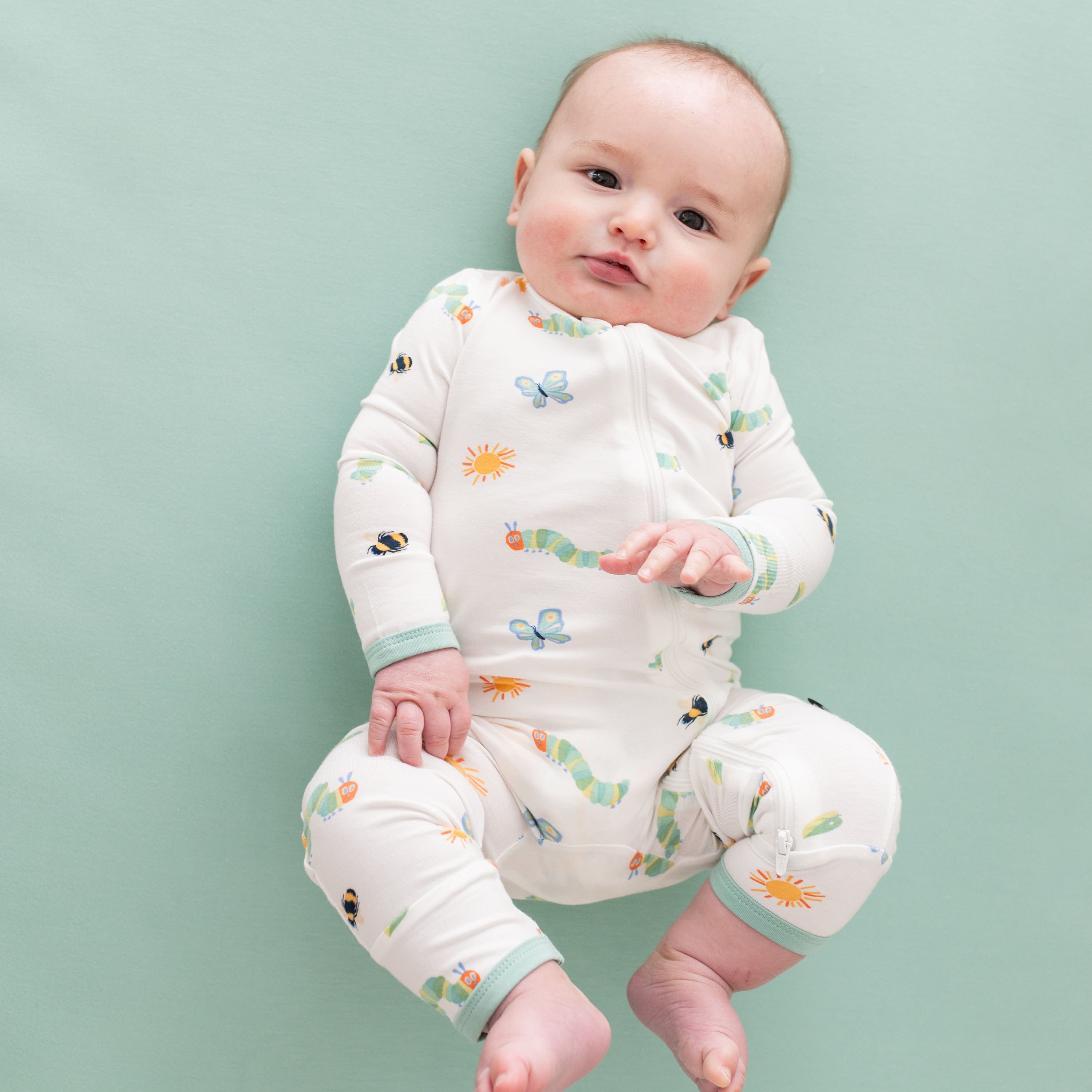 Young infant laying on a green crib sheet wearing the Zippered Romper in The Very Hungry Caterpillar™ and Friends
