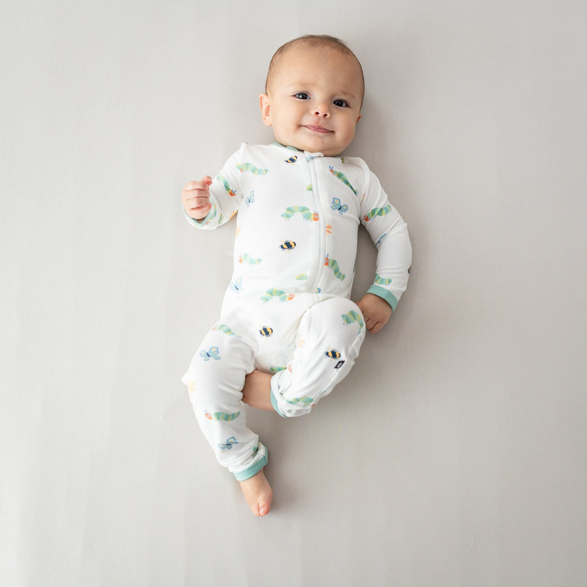 Young infant laying on a light beige blanket wearing the Zippered Romper in The Very Hungry Caterpillar™ and Friends