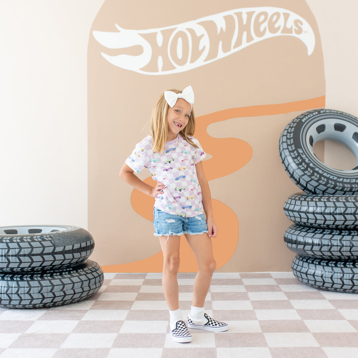 Girl model standing with hand on her hip wearing the Toddler Basic Tee in Sparkles and Speed paired with jean shorts