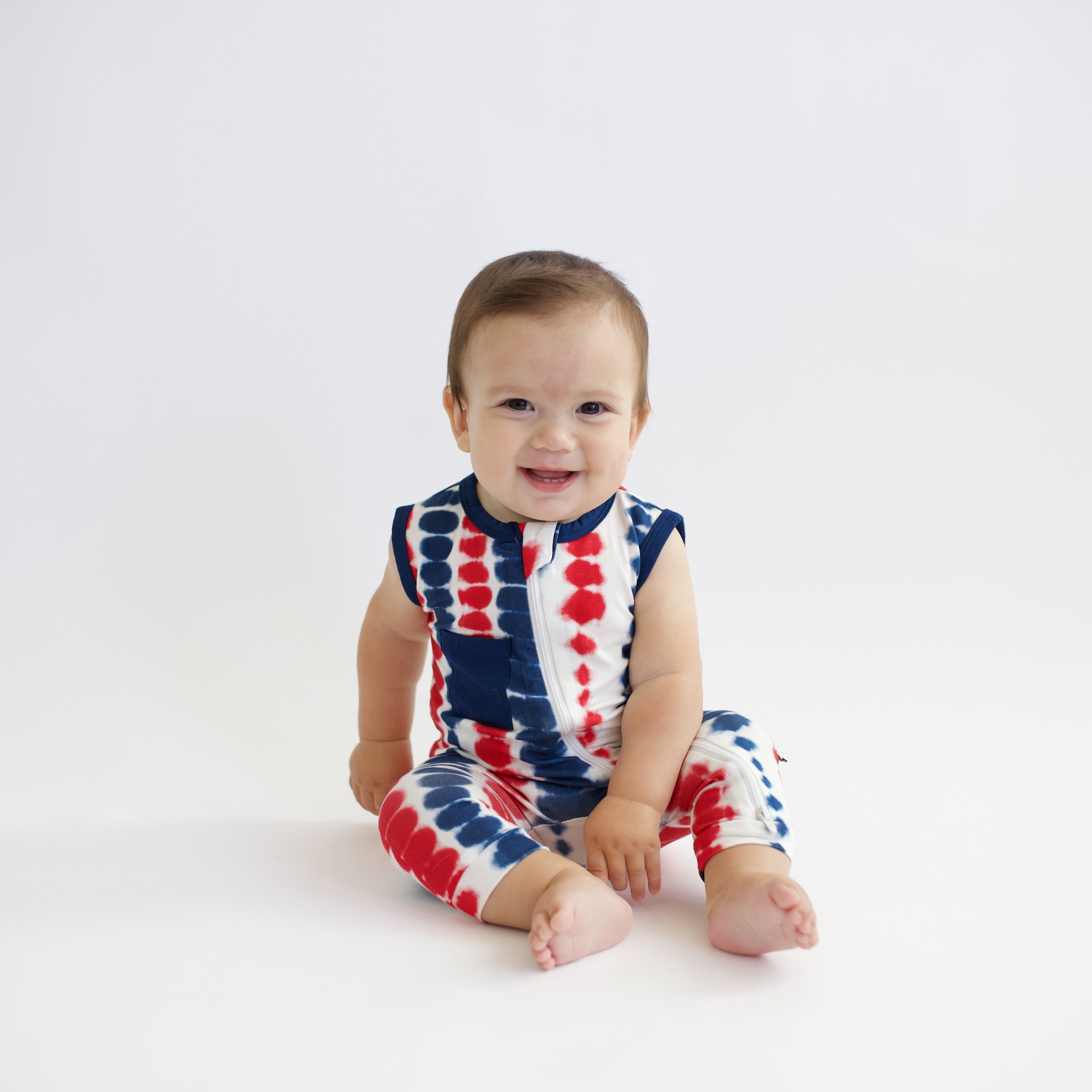 Baby sitting smiling wearing Zippered Sleeveless Romper in Liberty Rip Tide