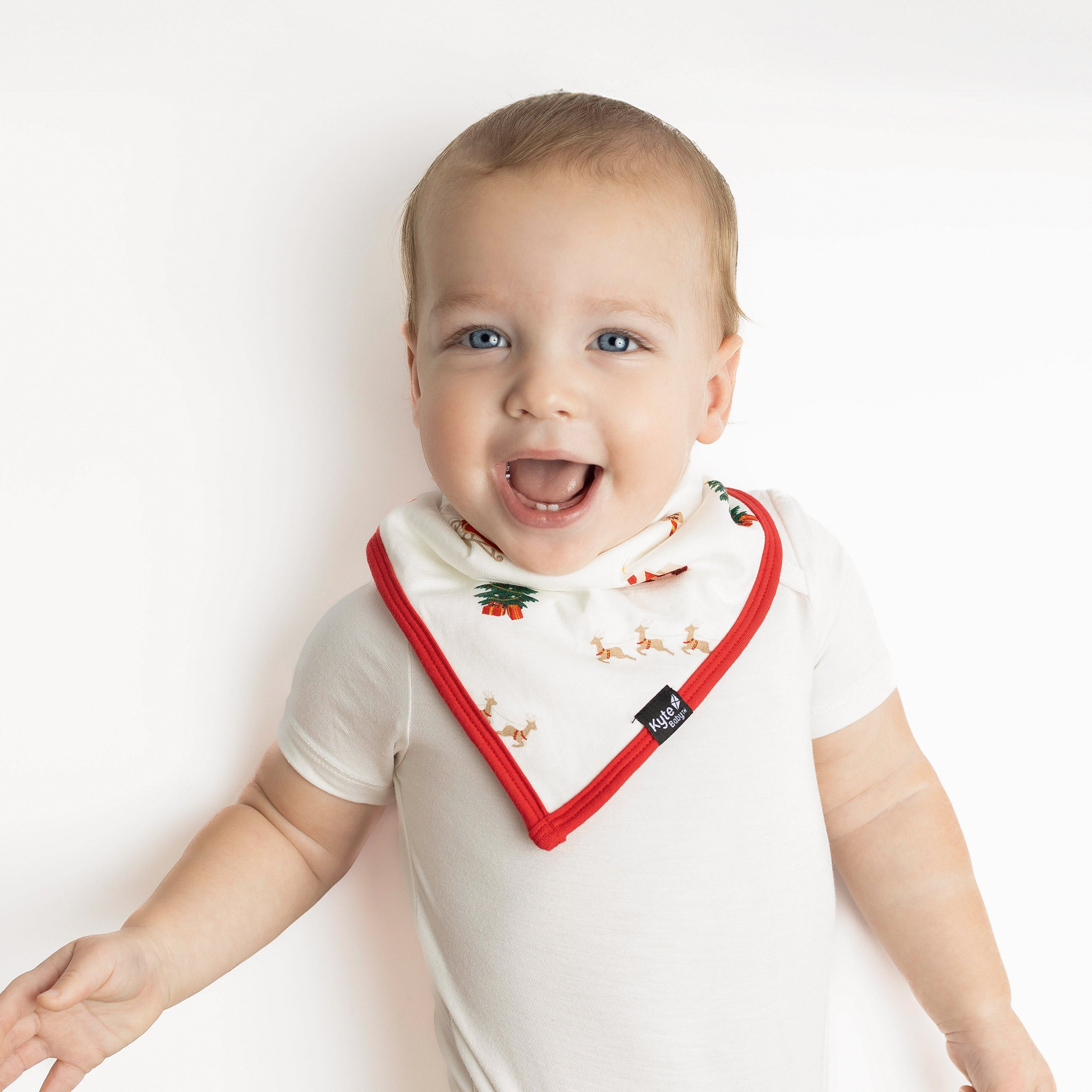 Smiling toddler laying down wearing the Bib in Santa Sleigh