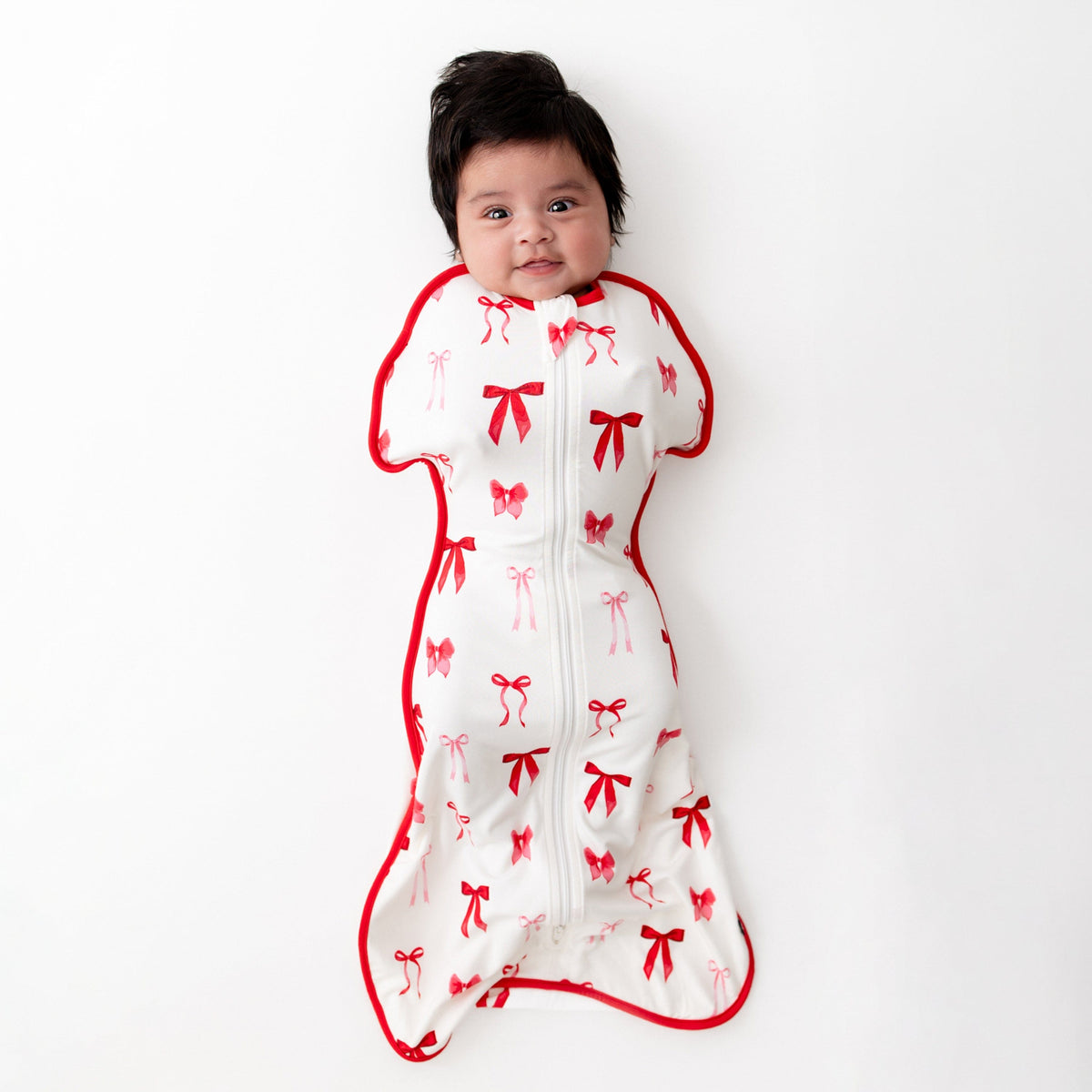 Infant laying on a white surface wearing the soft and stretchy Swaddle Bag in Small Love Bow 0.5