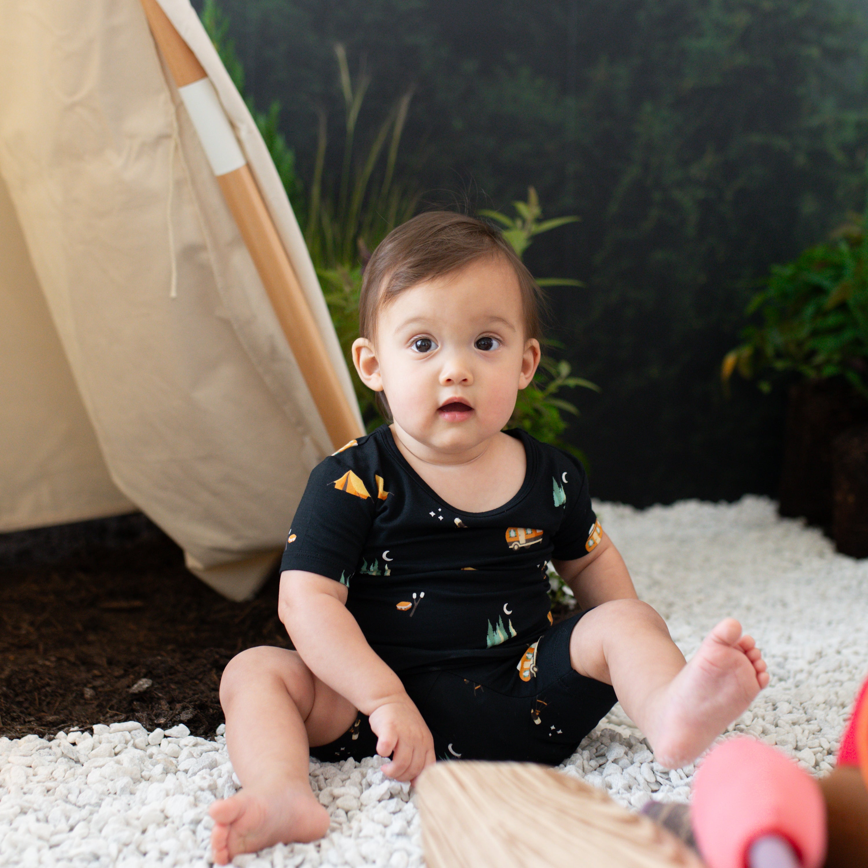 Infant sitting in the rocks wearing the Short Sleeve Pajamas in Under the Stars in a staged camping set