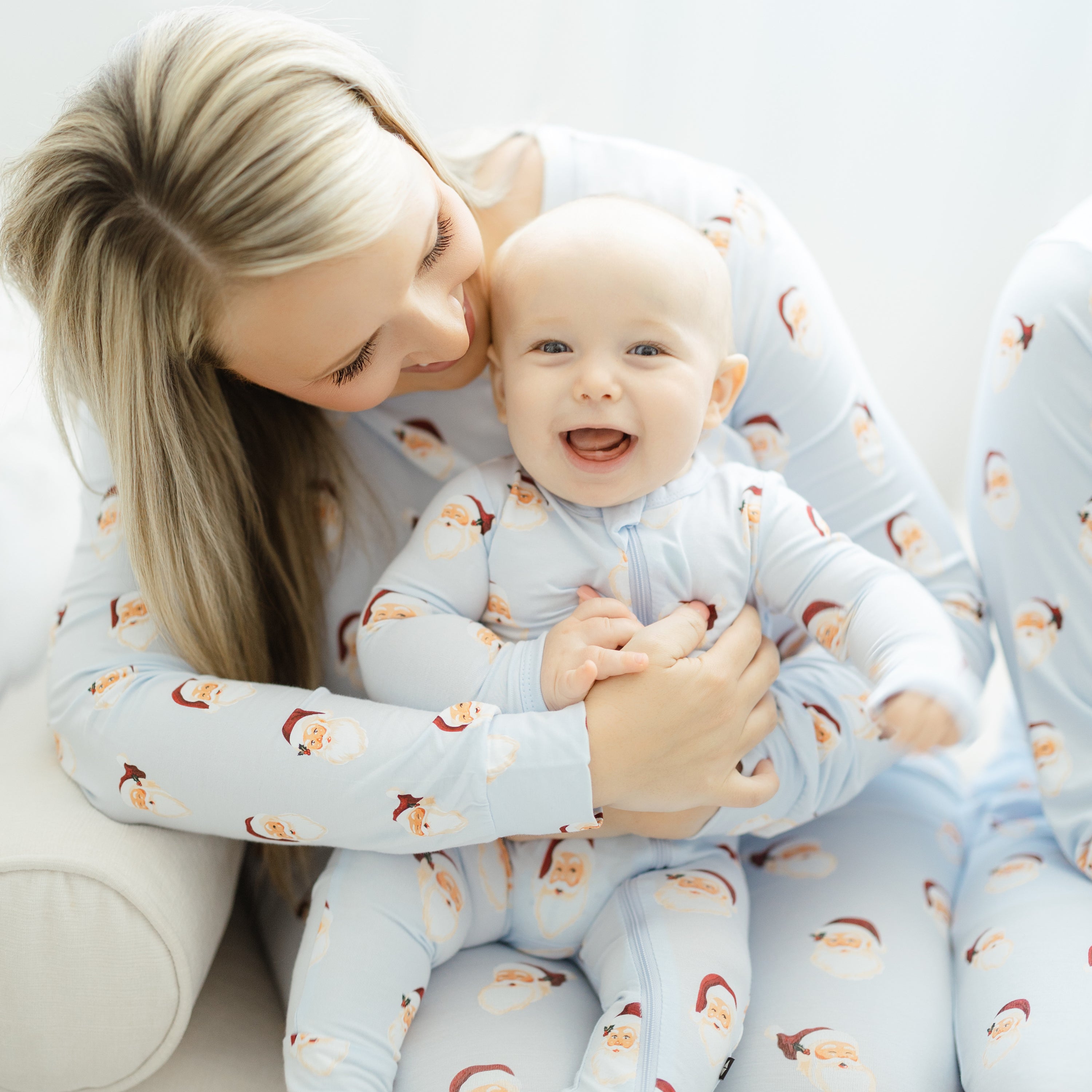 Close up of a smiling infant wearing the Zippered Romper in Vintage Santa sitting on their mother's lap who is matching in the Women's jogger set