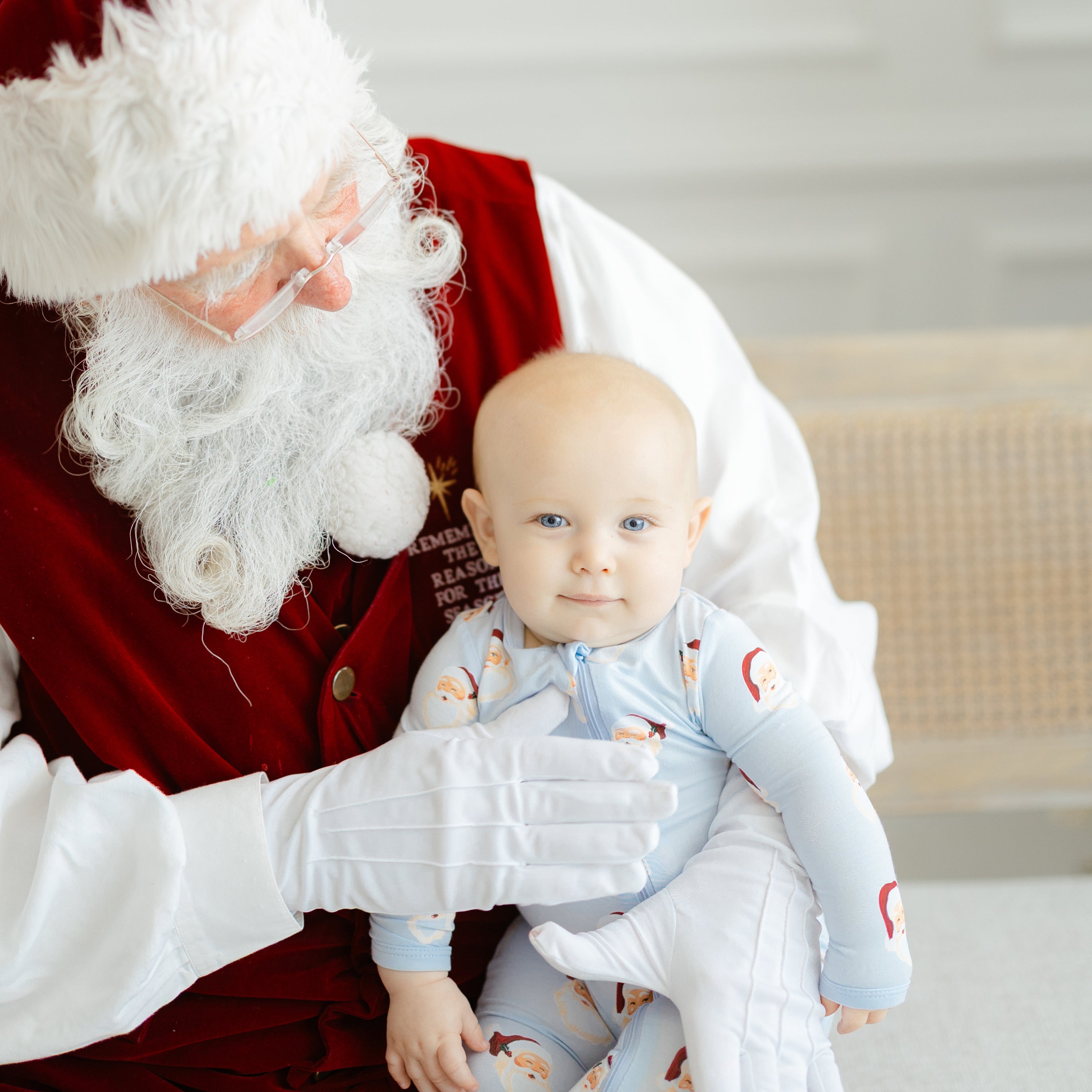 An infant wearing the Zippered Romper in Vintage Santa sitting on a Santa Clause lap