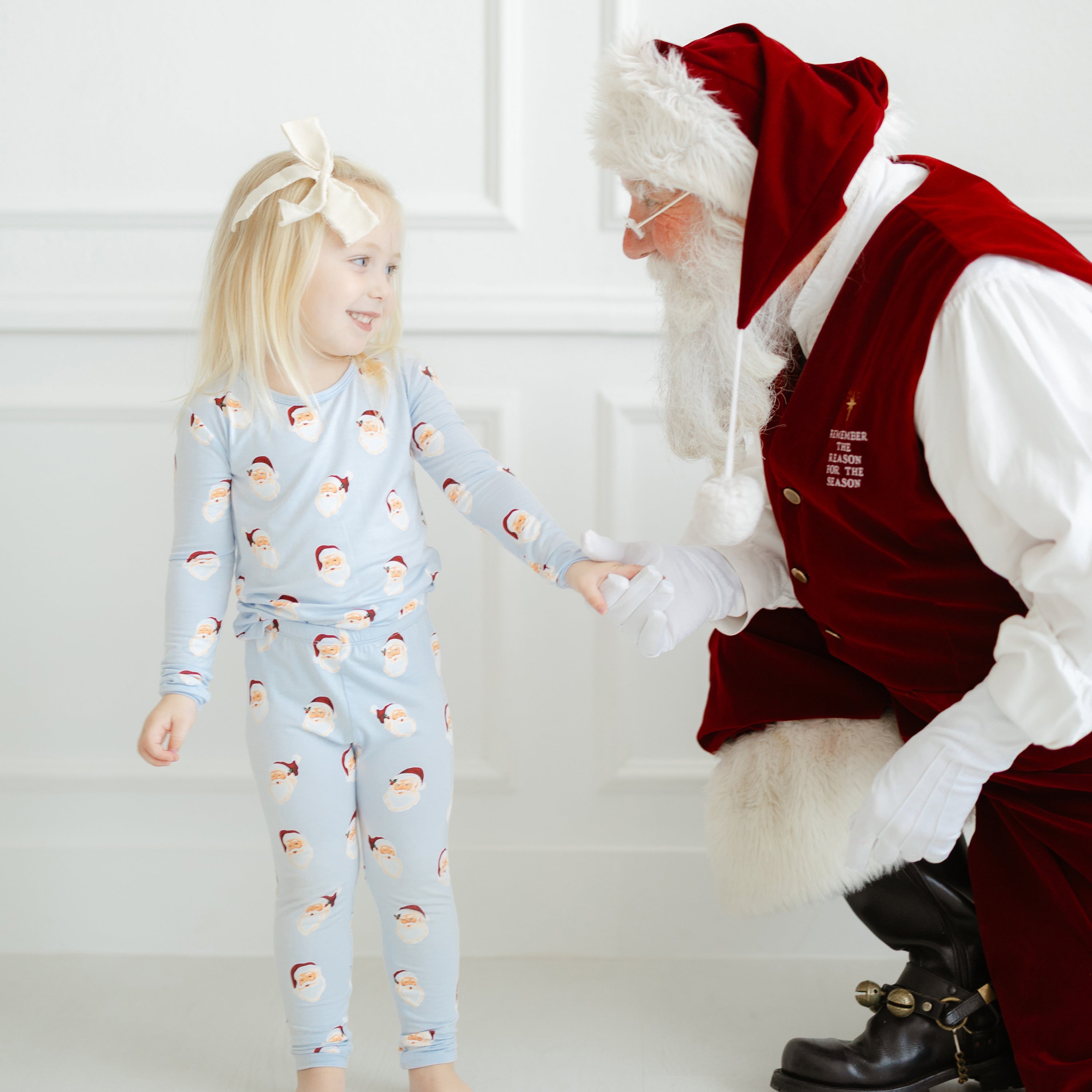 Young girl wearing the longs sleeve toddler pajama set in Vintage Santa smiling at and holding the hand of a santa clause