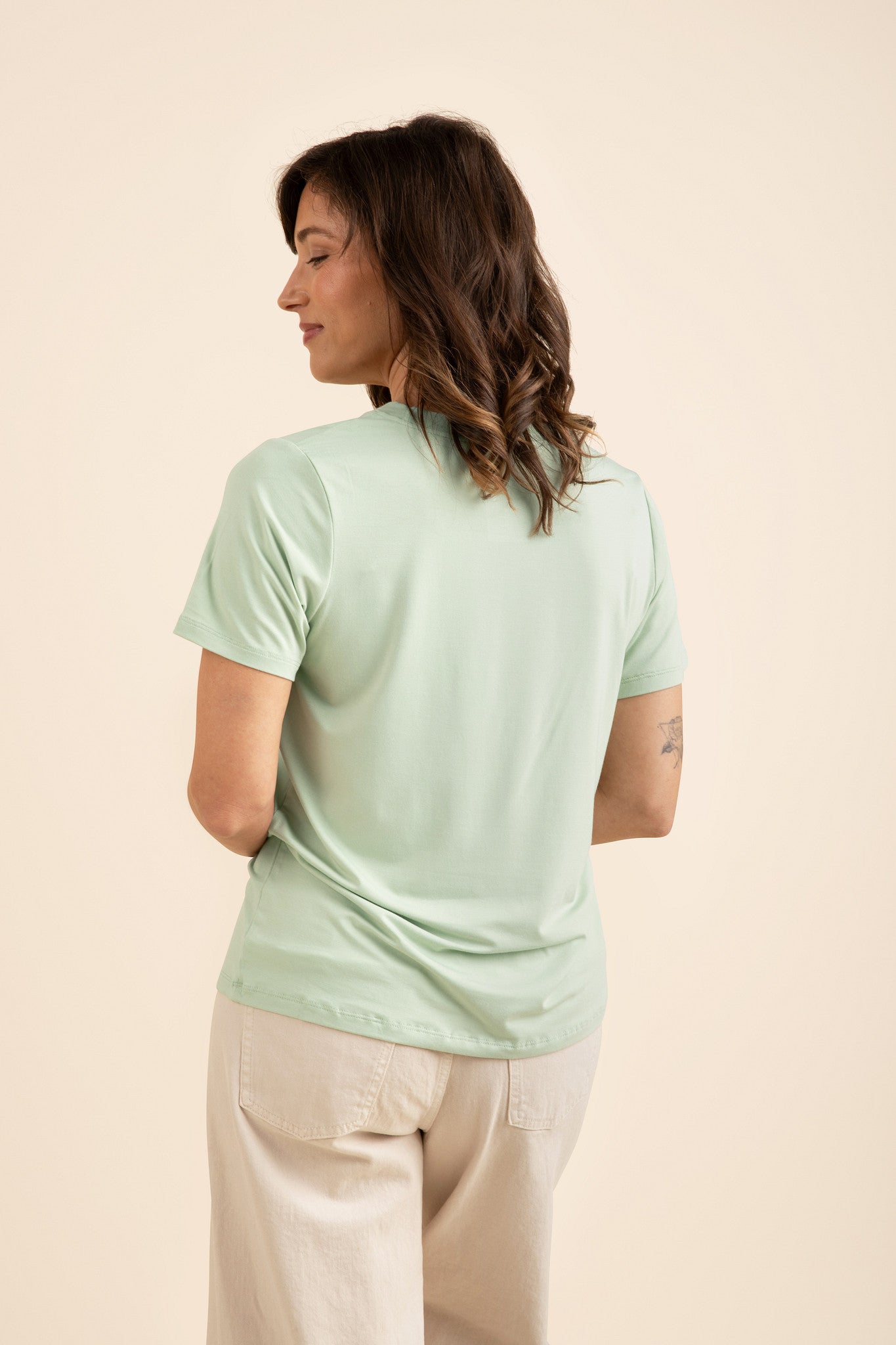 Woman wearing a light green t-shirt and cream pants against a beige background