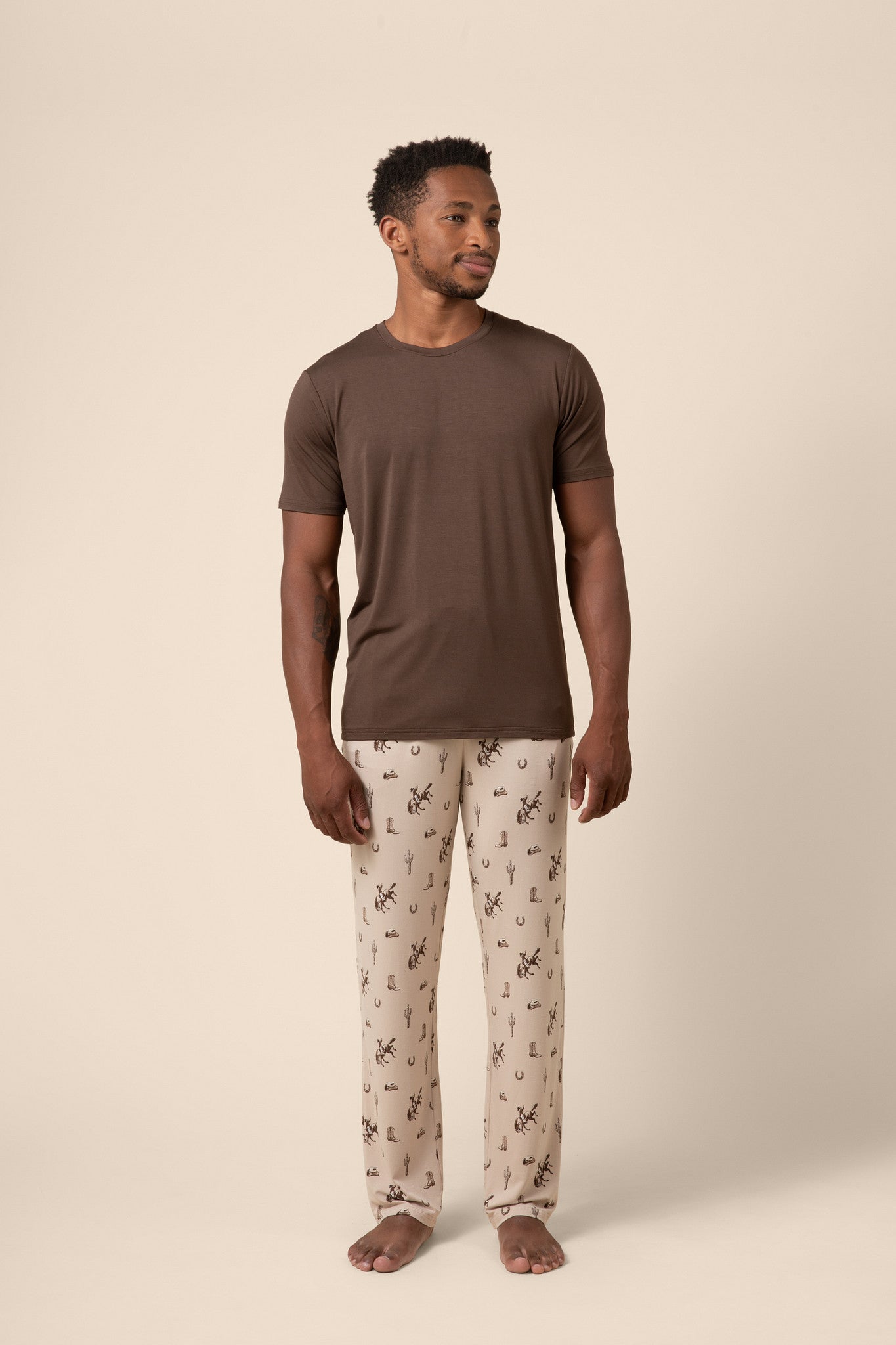 Man wearing a brown t-shirt and cowboy patterned pajama pants on a beige background
