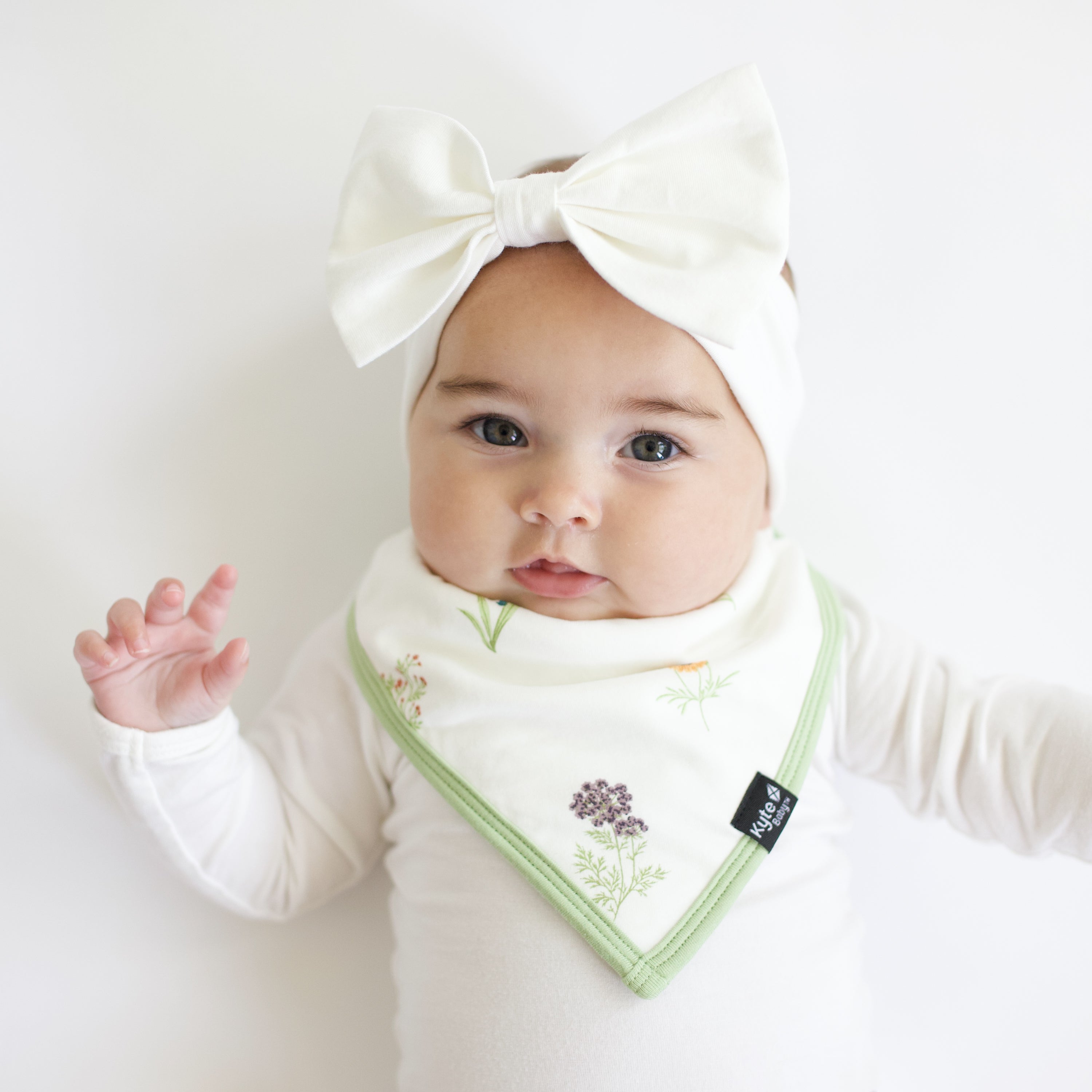 Infant wearing white bodysuit and bow headband with Wildflower bib