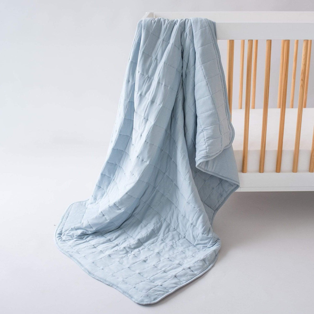 Toddler Blanket in Fog 2.5 TOG draped over a white and gold crib