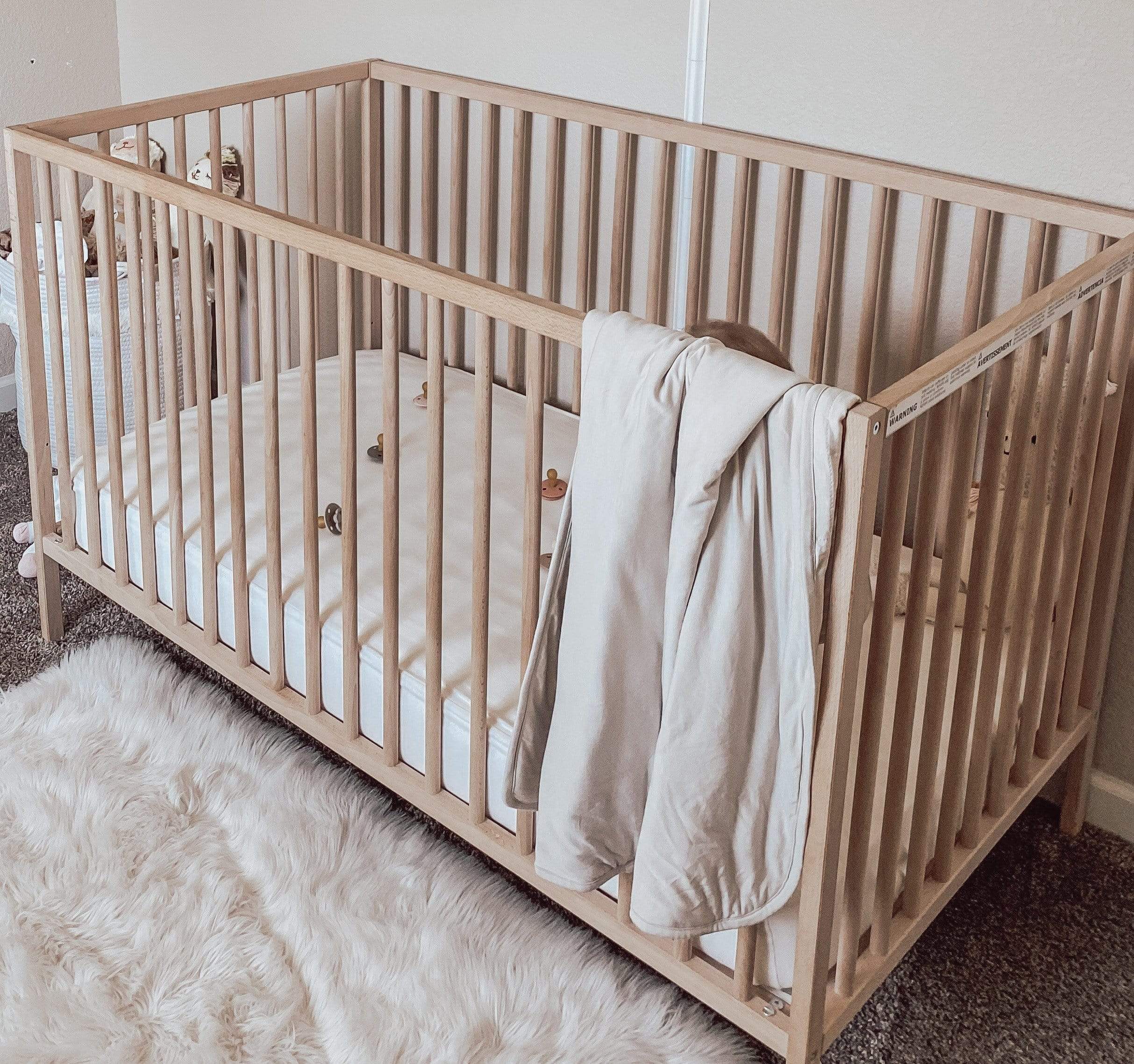 Wooden crib with Baby Blanket in Oat 1.0 TOG draped over the front rail