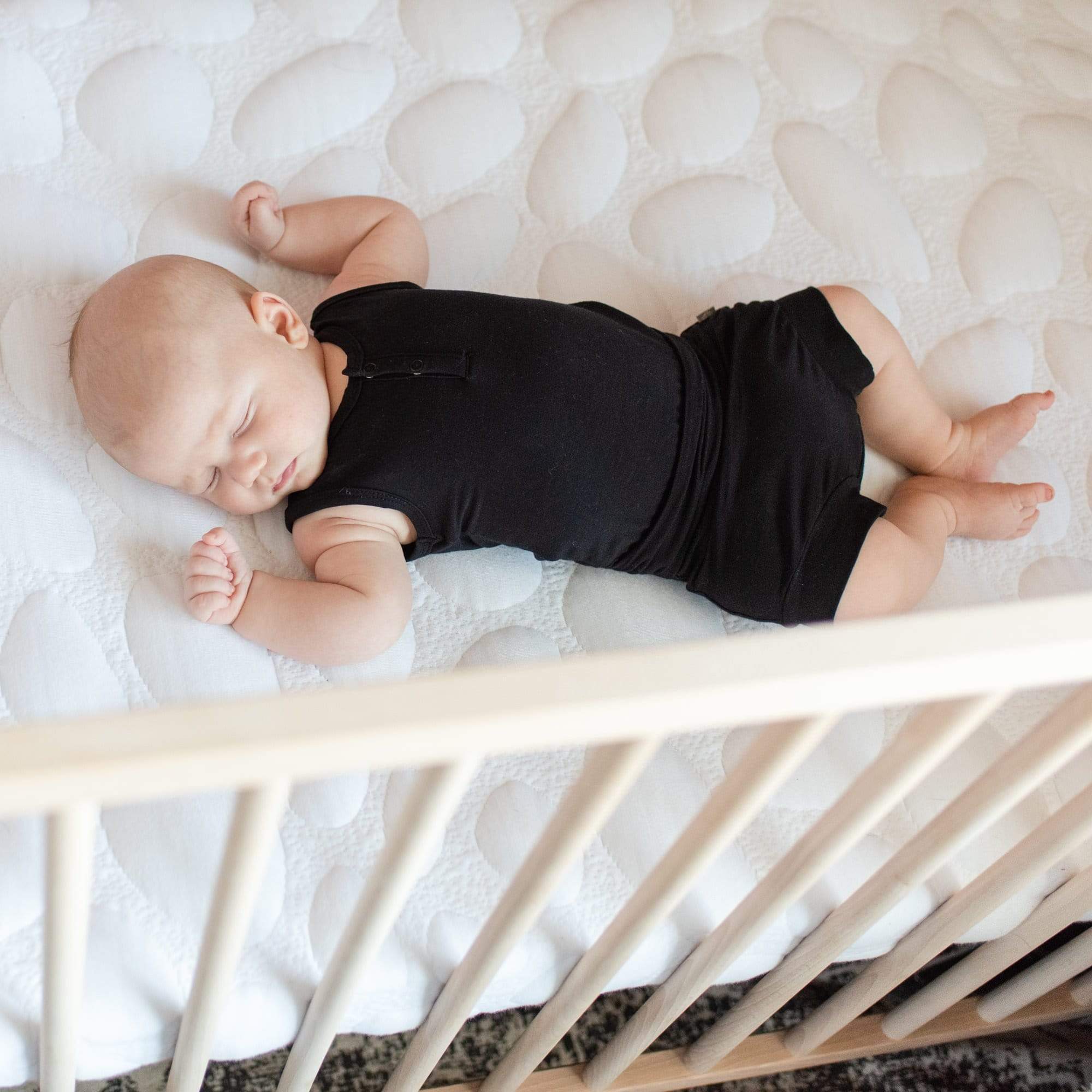Infant sleeping in Kyte Baby Bummies in Midnight while laying in a crib