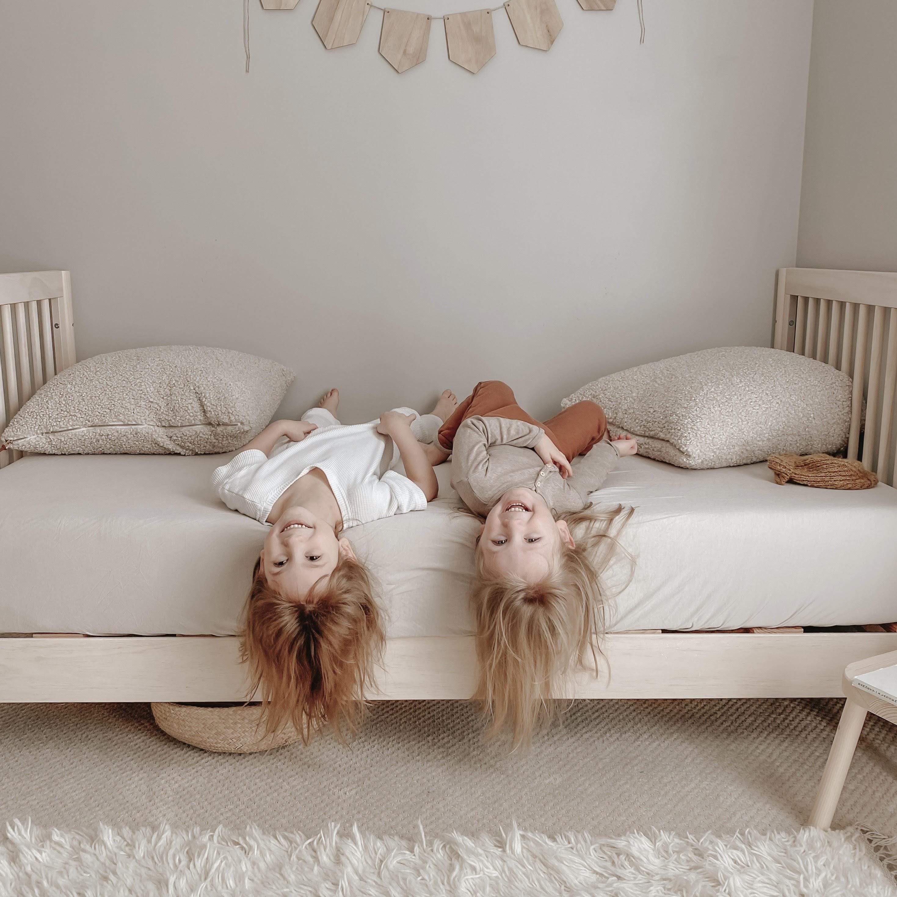 Kids playing on bed with Kyte Baby Twin fitted sheet in Oat