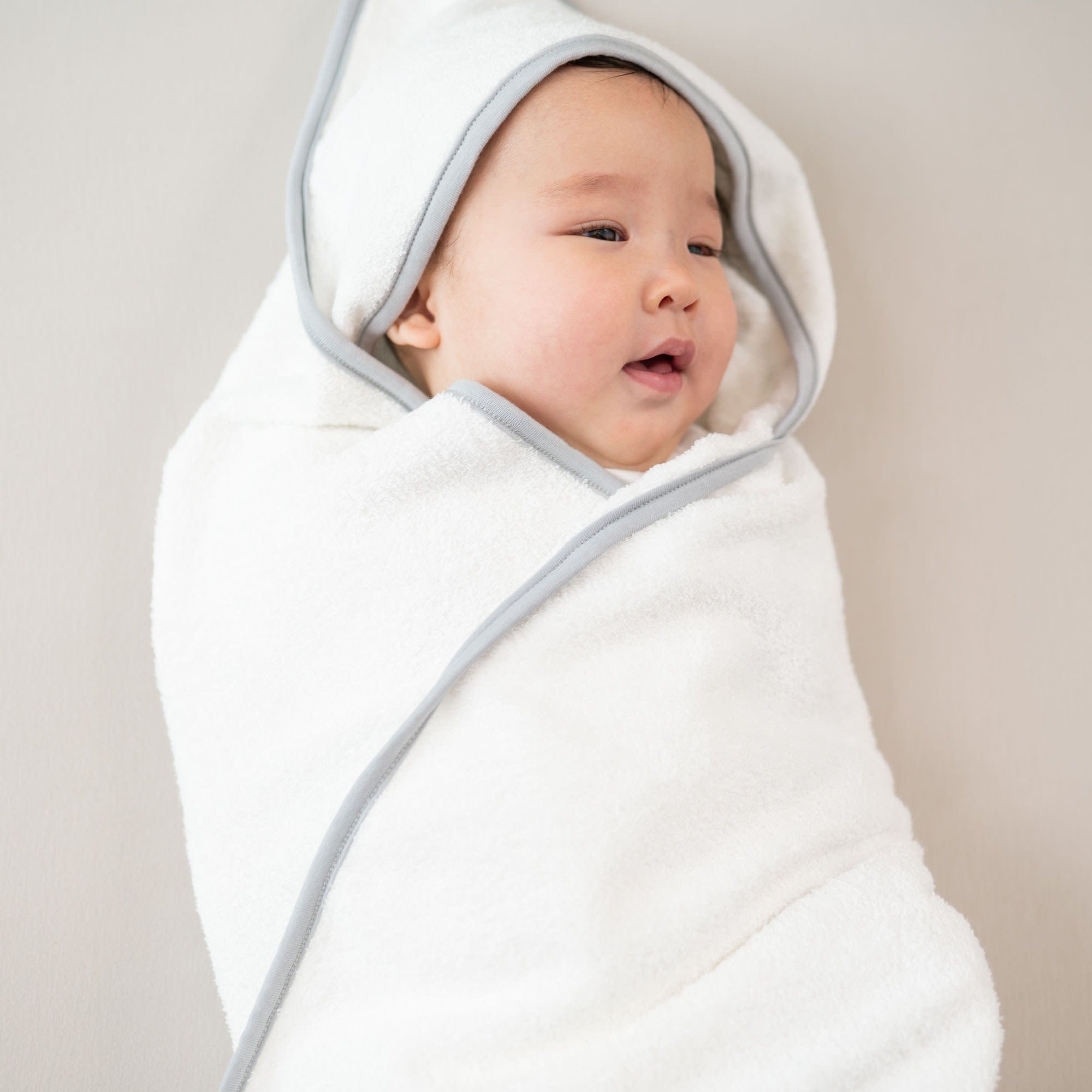 Infant wrapped in Kyte Baby bamboo terry Hooded Bath Towel in Cloud with Storm Trim