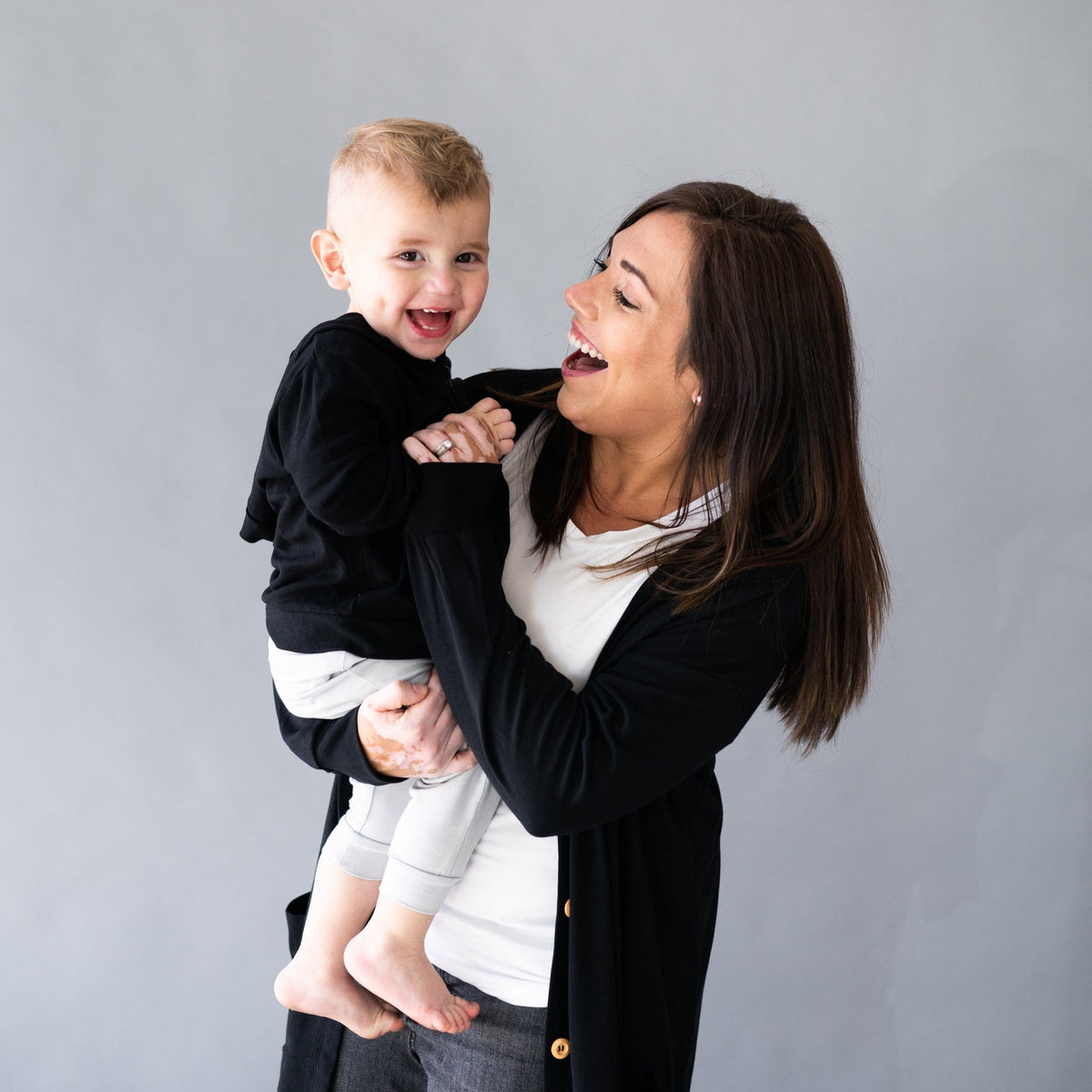 Mom holding toddler wearing Kyte Baby Bamboo Jersey Hooded Jacket in Midnight black