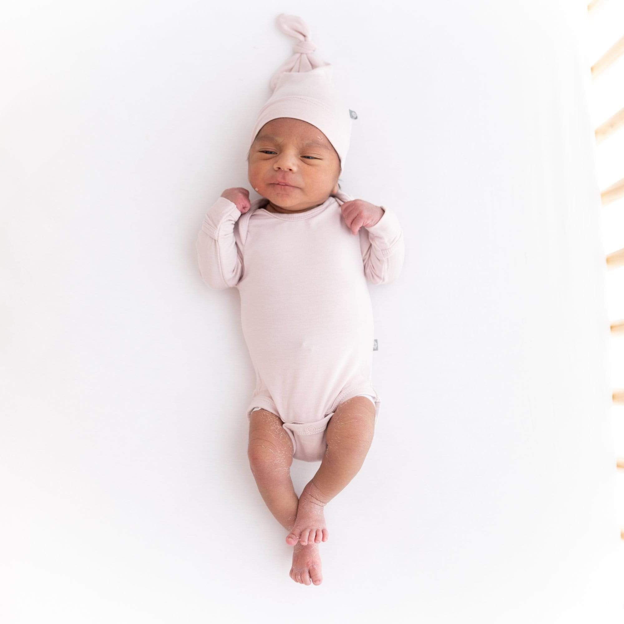 Newborn wearing Kyte Baby Knotted Cap in Blush and matching long sleeve bodysuit