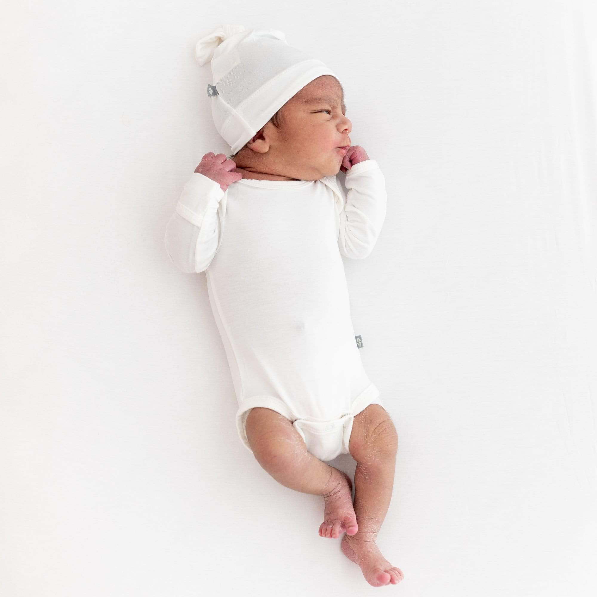 Infant laying on white surface in Kyte Baby bamboo Knotted Cap in Cloud and cloud bodysuit