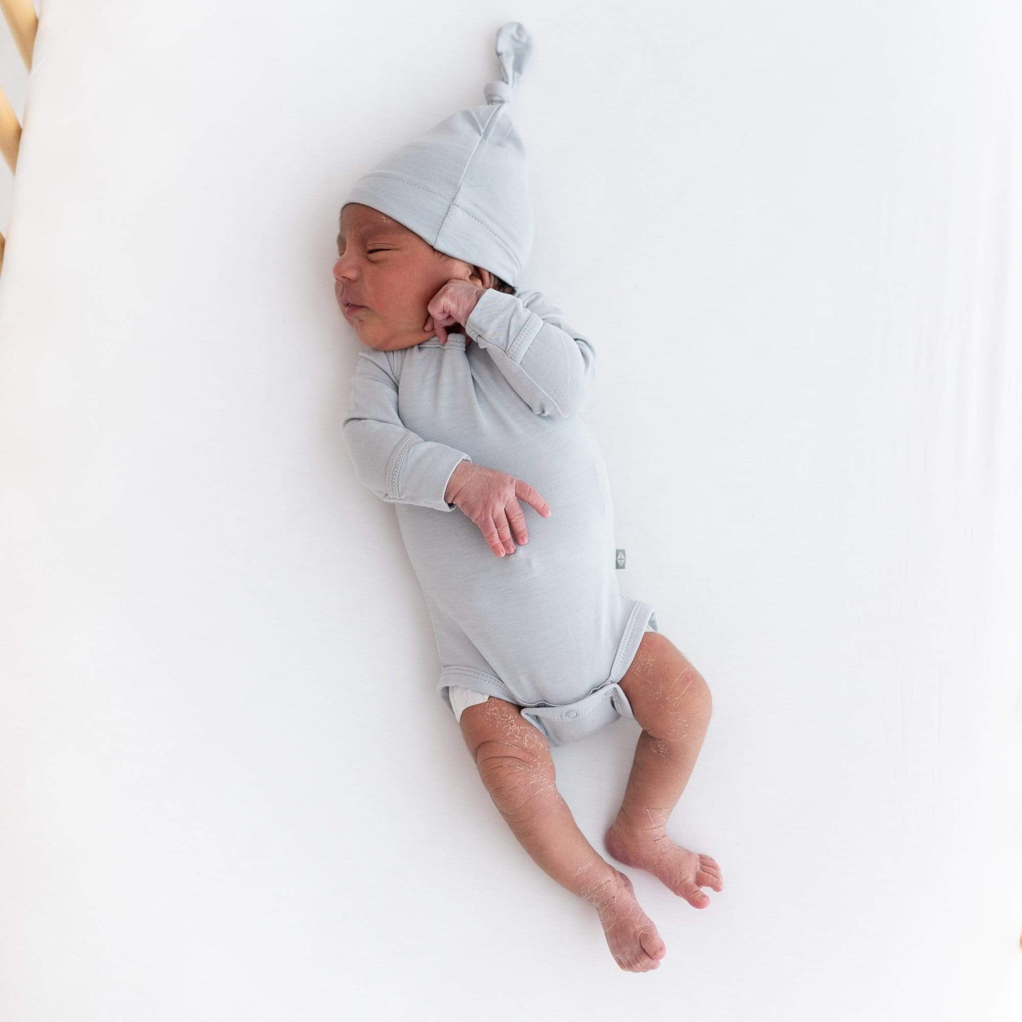 Newborn sleeping on a Crib Sheet in Cloud while wearing a Knotted Cap and Long Sleeve Bodysuit in Slate