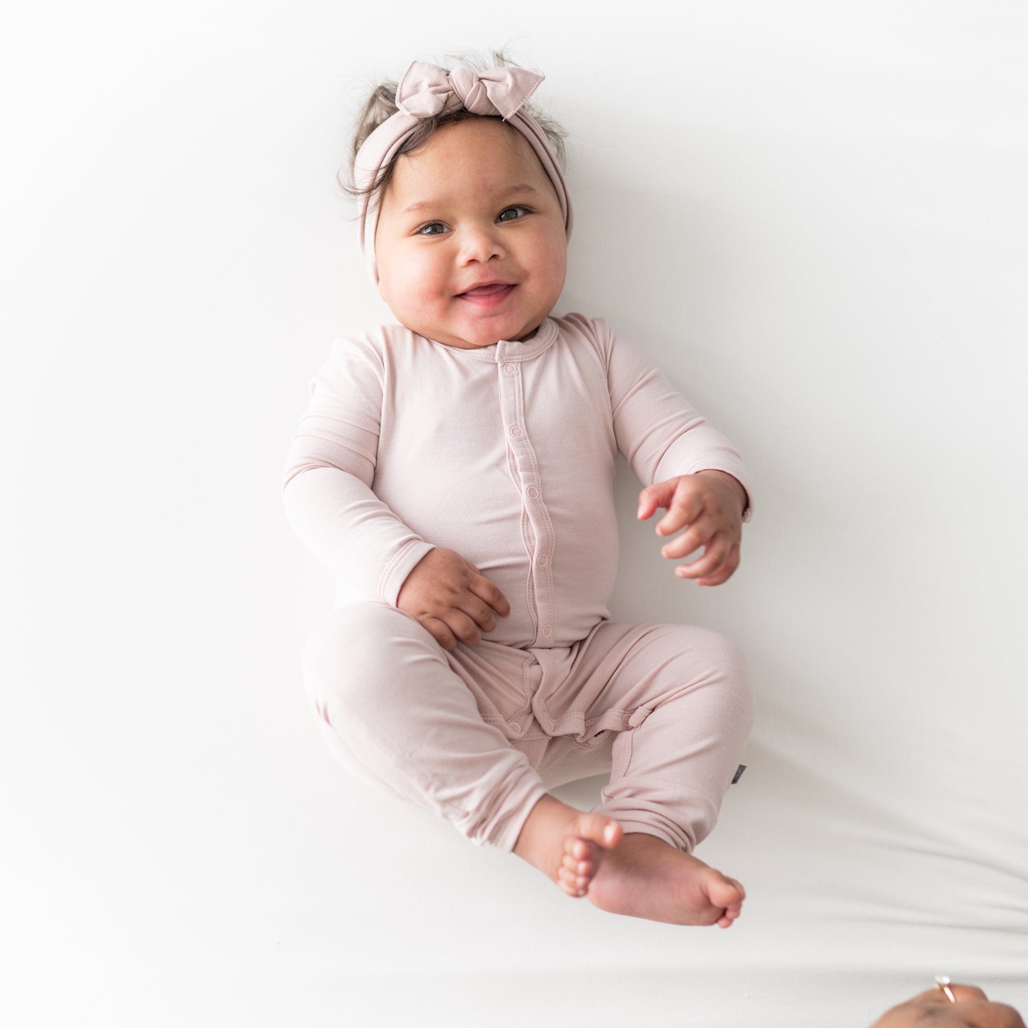 Smiling baby wearing Kyte Baby Romper in Blush and matching bow headband