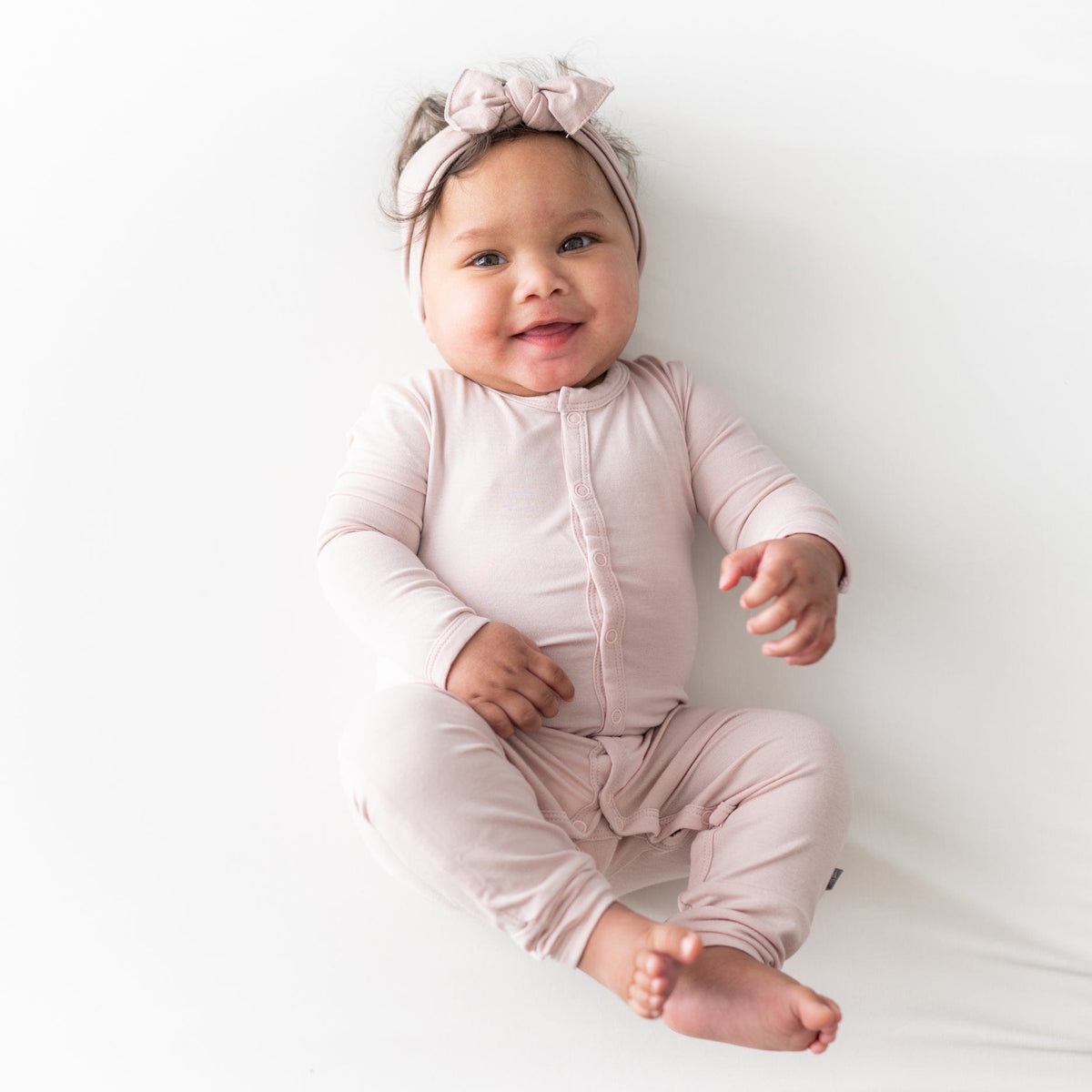 Smiling baby wearing Kyte Baby Romper in Blush and matching bow headband