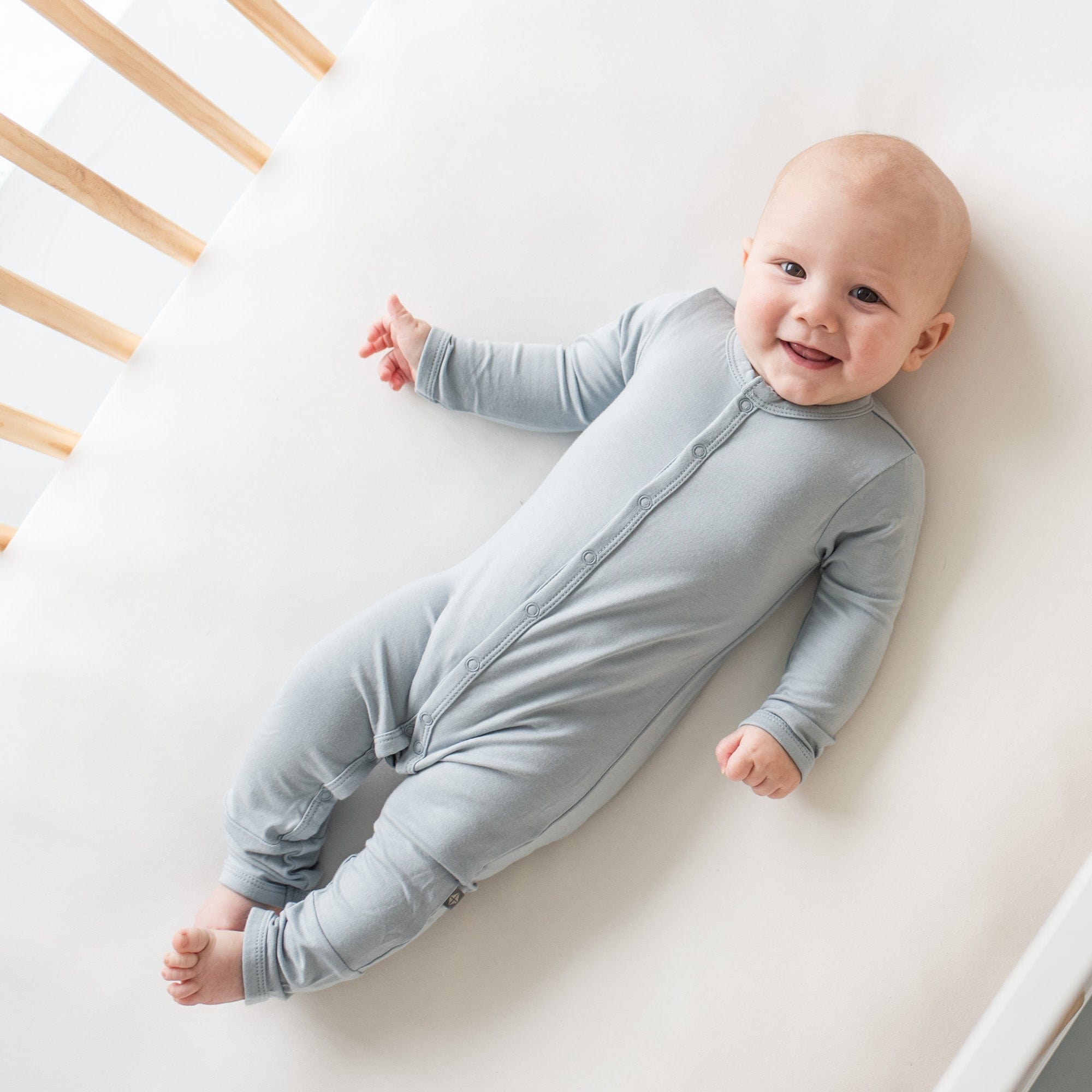 Smiling infant in a crib wearing Kyte Baby Romper in Fog
