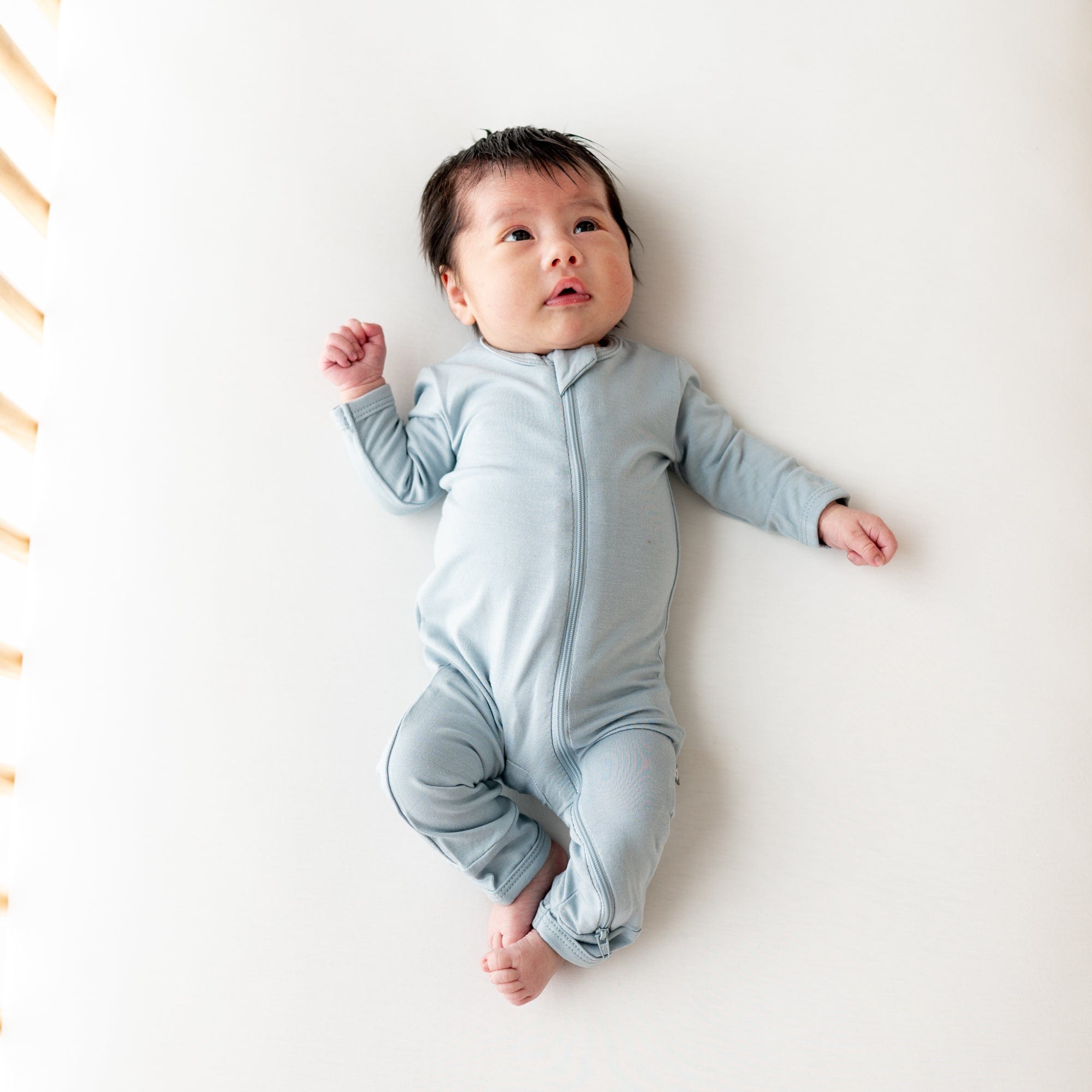 Infant laying in a crib while wearing a Zippered Romper in Fog