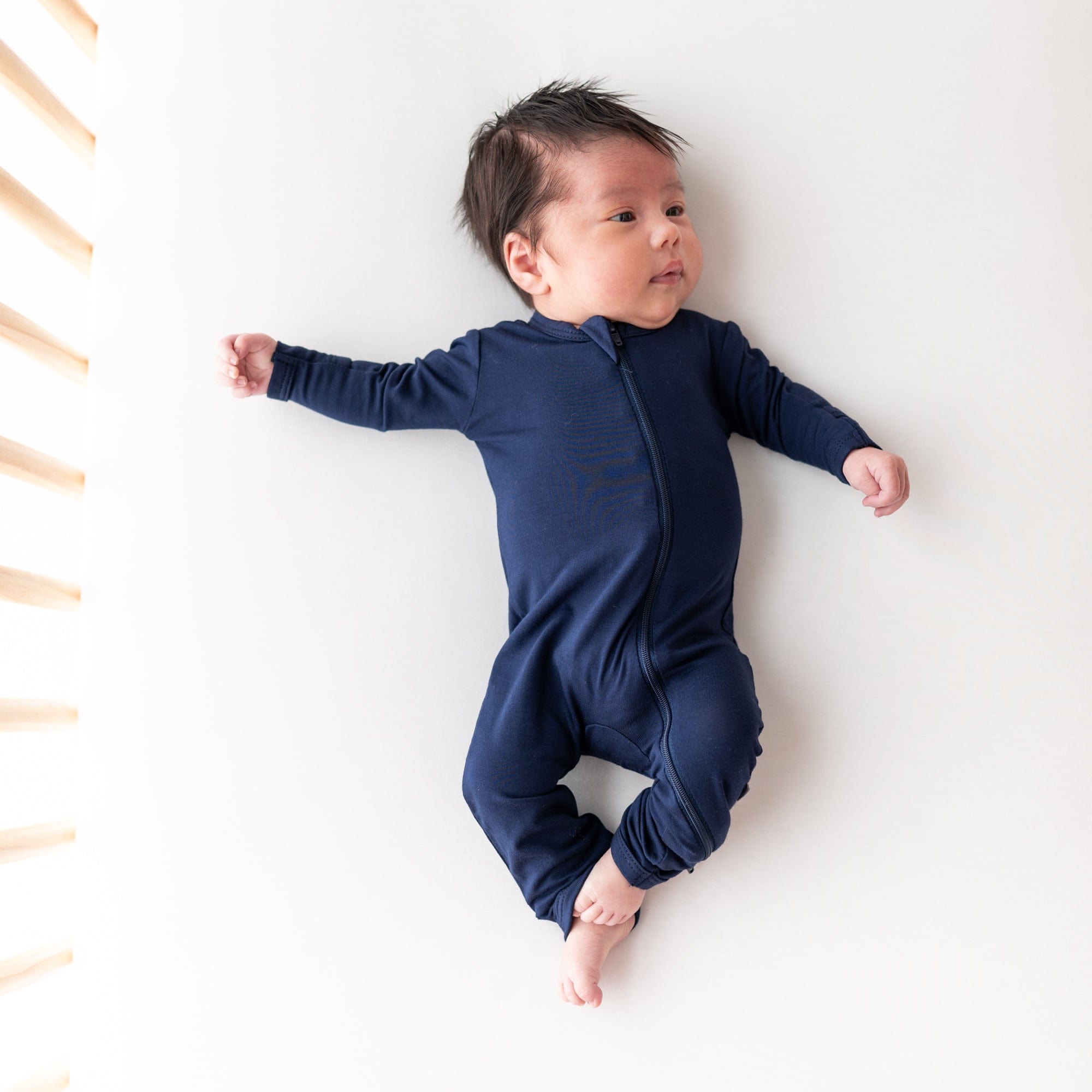 Infant laying in a crib while wearing a Zippered Romper in Navy