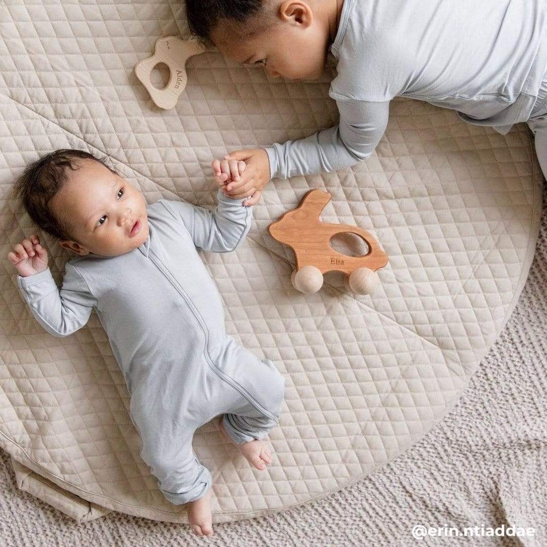 Siblings laying on a quilted, beige playmat holding hands and wearing matching pajamas in Storm