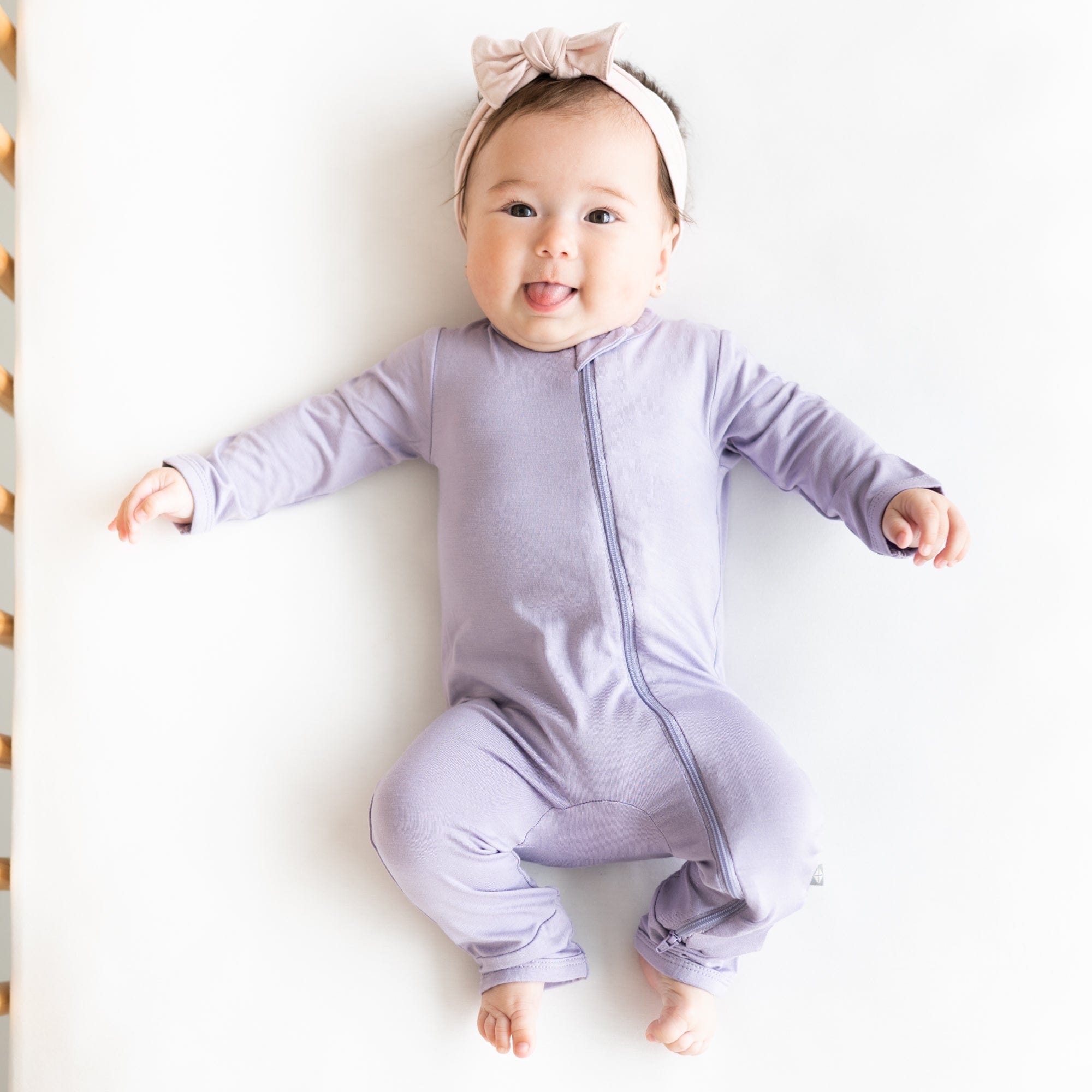 Infant wearing Ziippered Romper in Taro with a headband in Blush