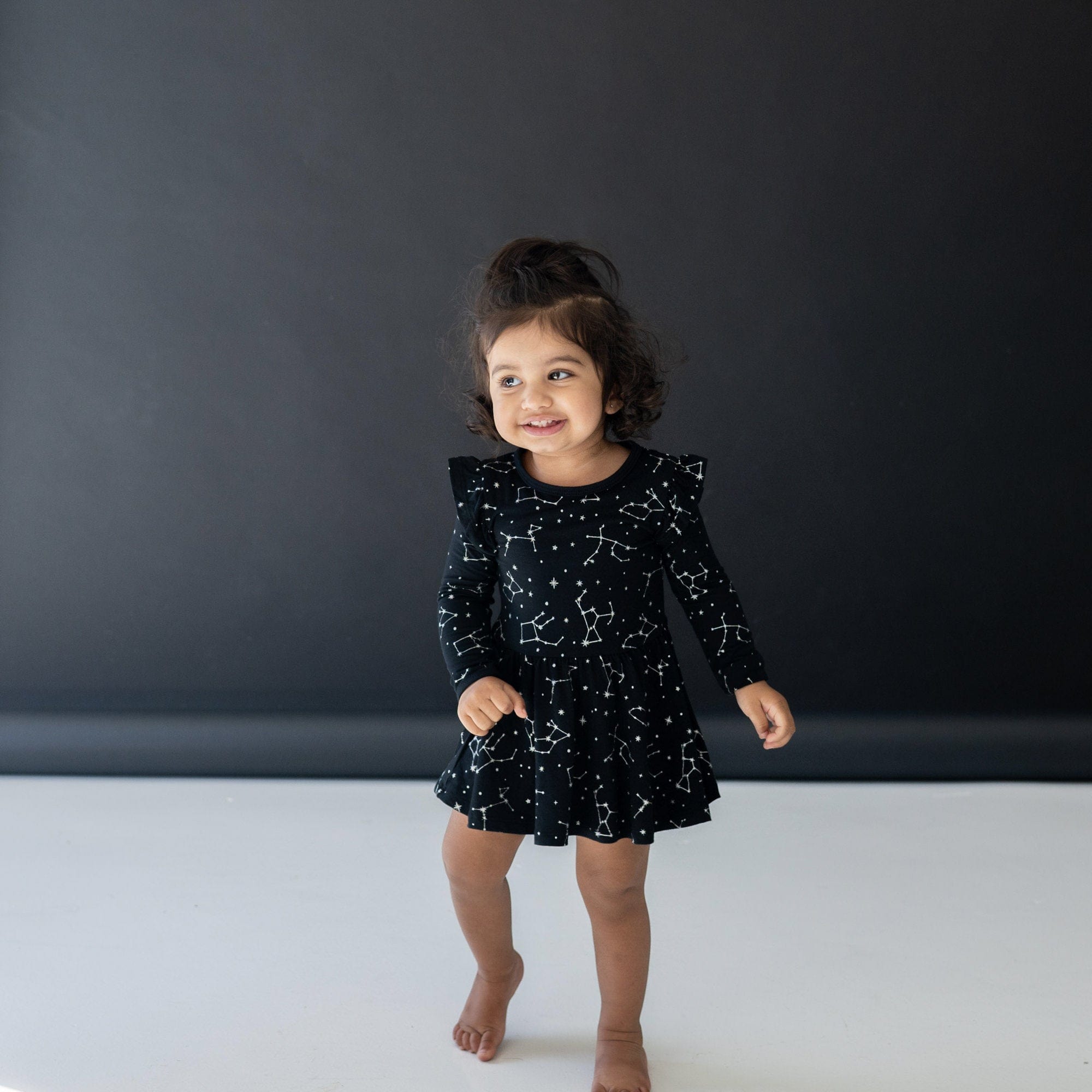 Girl wearing Kyte Baby bamboo Long Sleeve Twirl Bodysuit Dress in Midnight Constellations