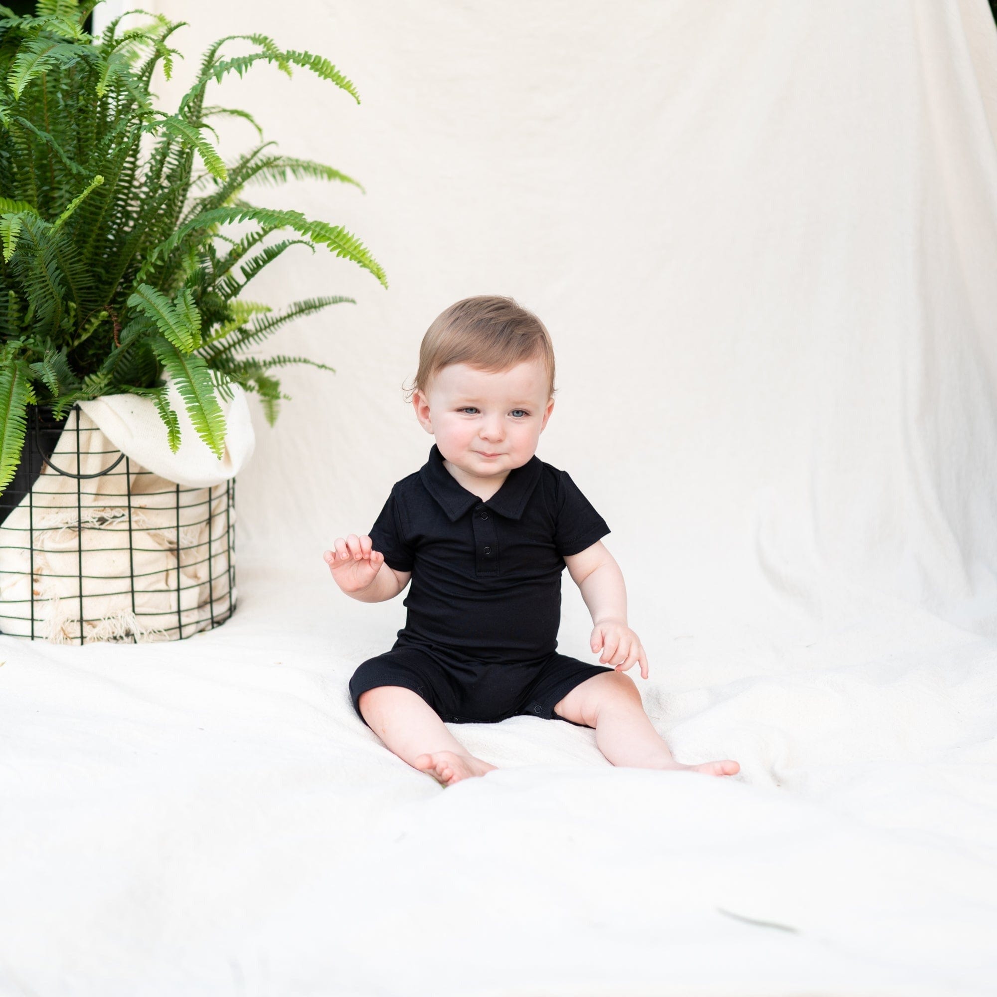 Infant wearing Kyte Baby Polo Shortall with snap closure in Midnight
