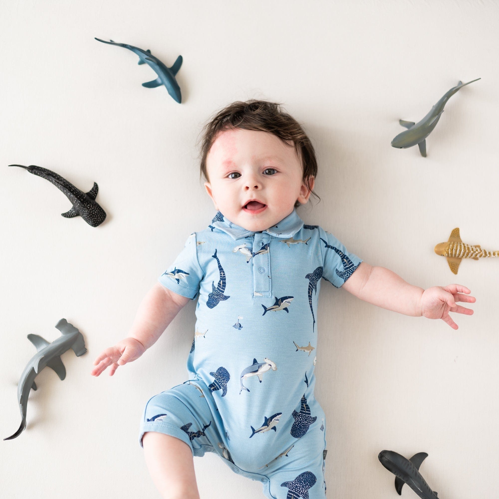 Infant wearing Kyte Baby Polo Shortall with snap closure in Stream Shark