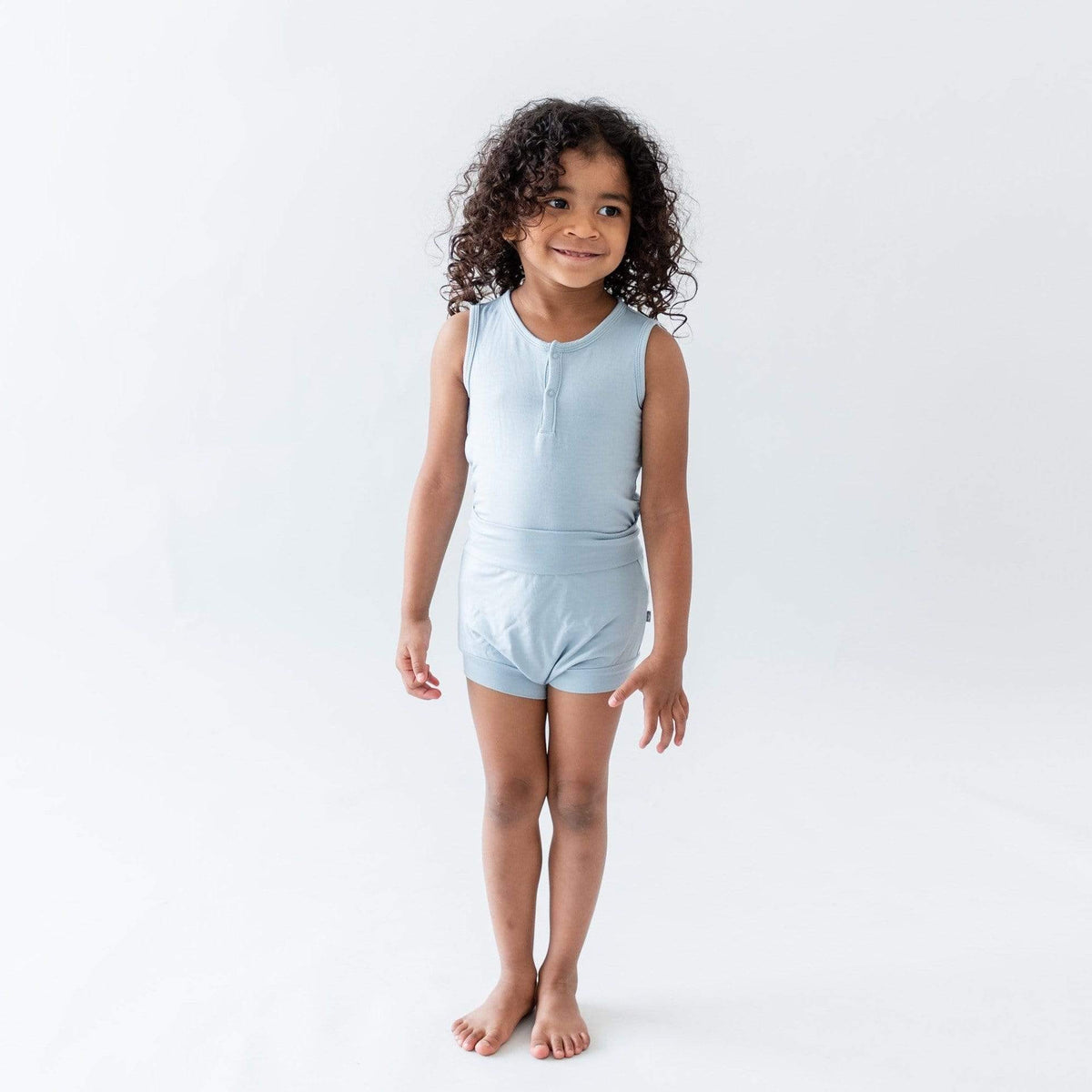 Standing toddler wearing Kyte Baby Sleeveless Bodysuit in Fog with matching bottoms