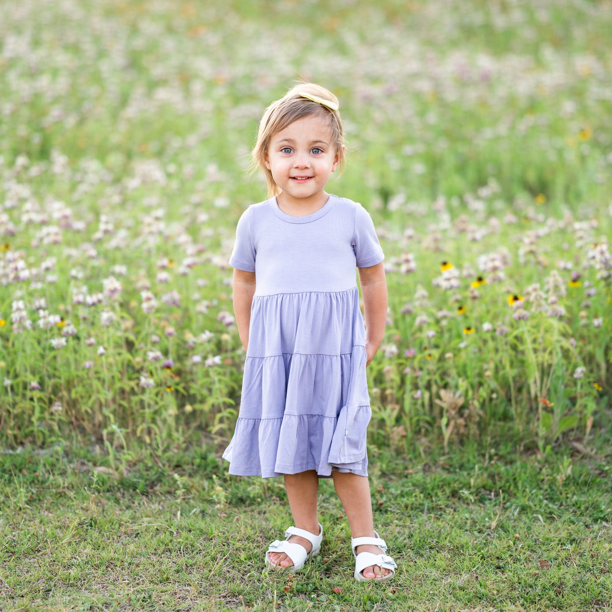 Girl standing in front of a field of wild flowers while wearing a Short Sleeve Tiered Dress in Taro