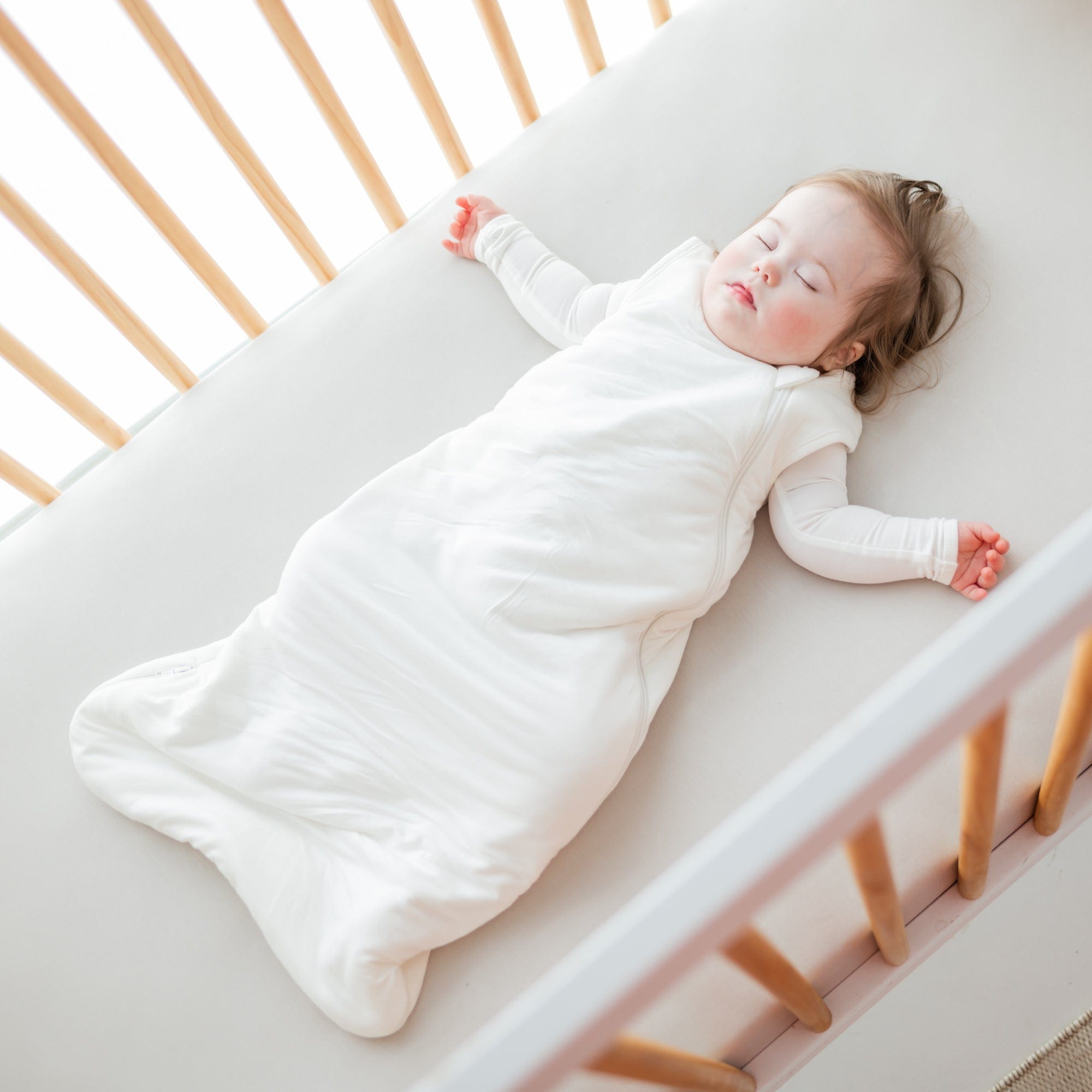 Sleeping baby laying in crib on a Crib Sheet in Oat while wearing Kyte Baby Sleep Bag in Cloud 1.0