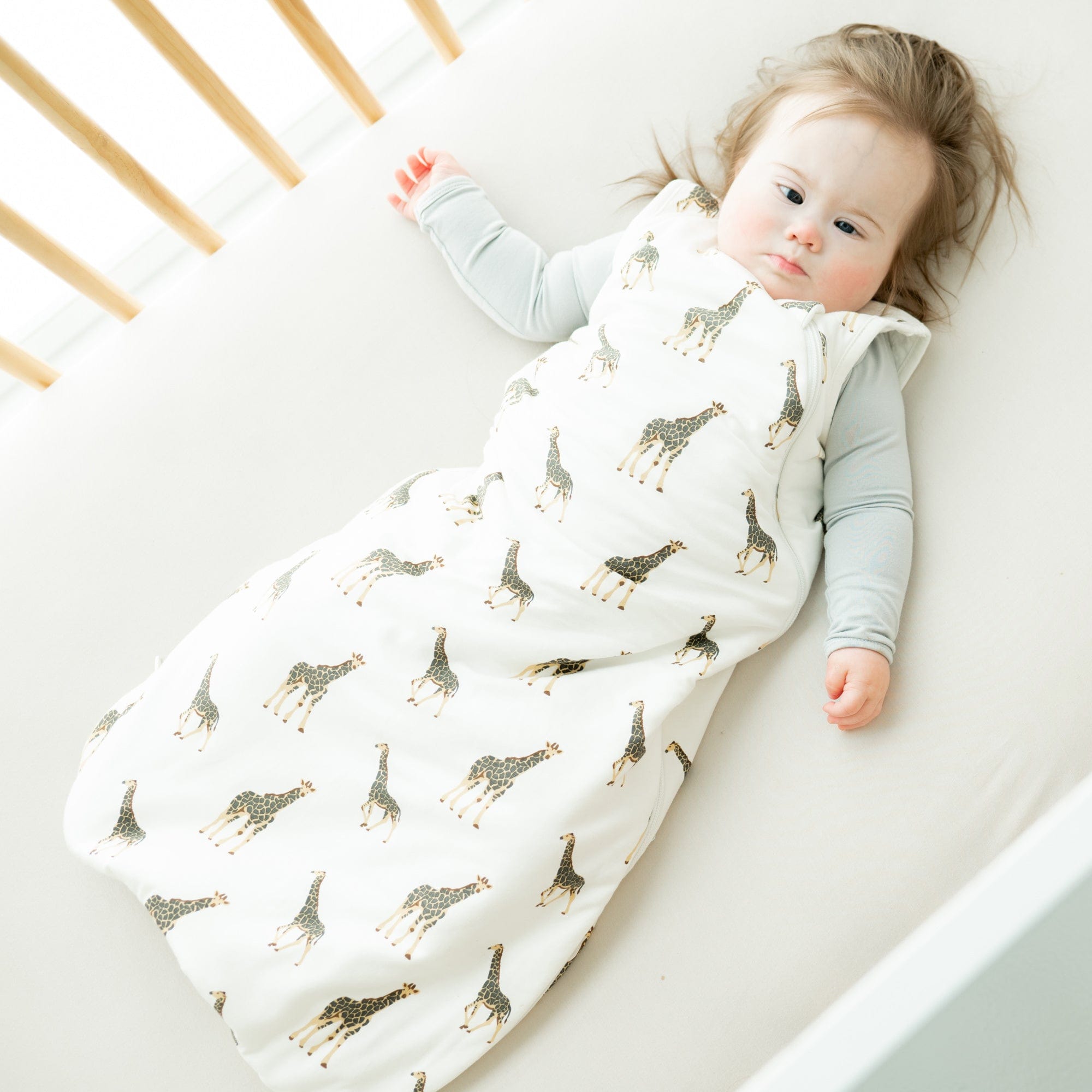 Baby wearing Kyte Baby bamboo Sleep Bag in Giraffe 1.0 laying on a Cloud crib sheet