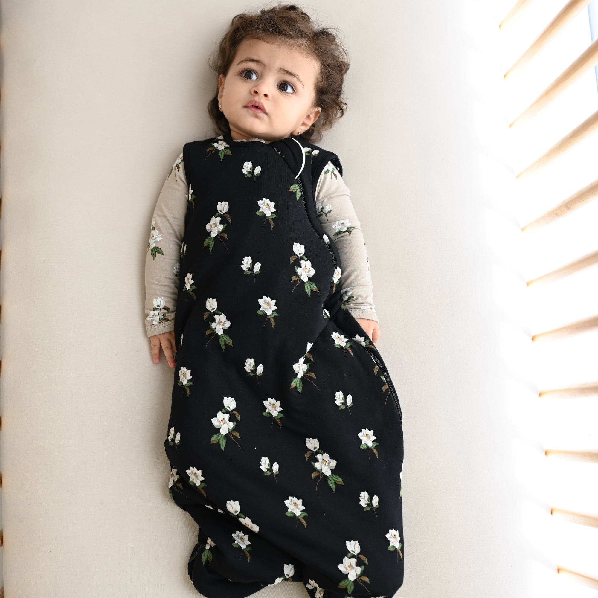 Infant wearing Kyte Baby Sleep Bag in Small Midnight Magnolia 1.0 with Khaki Magnolia long sleeve romper underneath