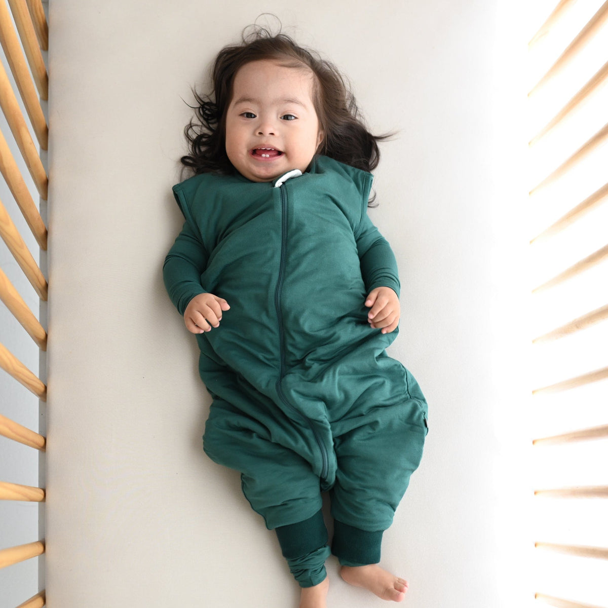 Toddler laying in crib while wearing a Kyte Baby Sleep Bag Walker in Emerald 1.0