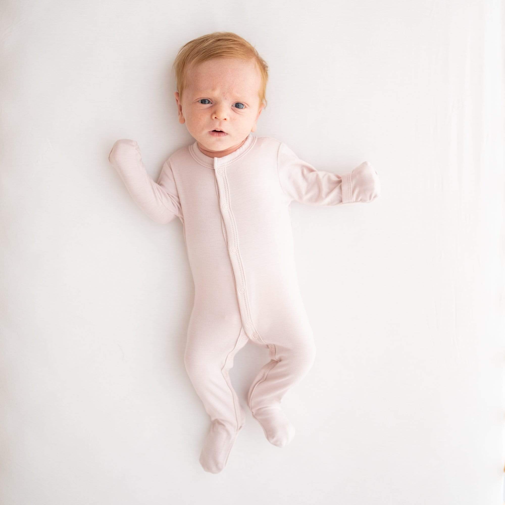 Infant wearing Footie in Blush with fold over cuffs being used on hands