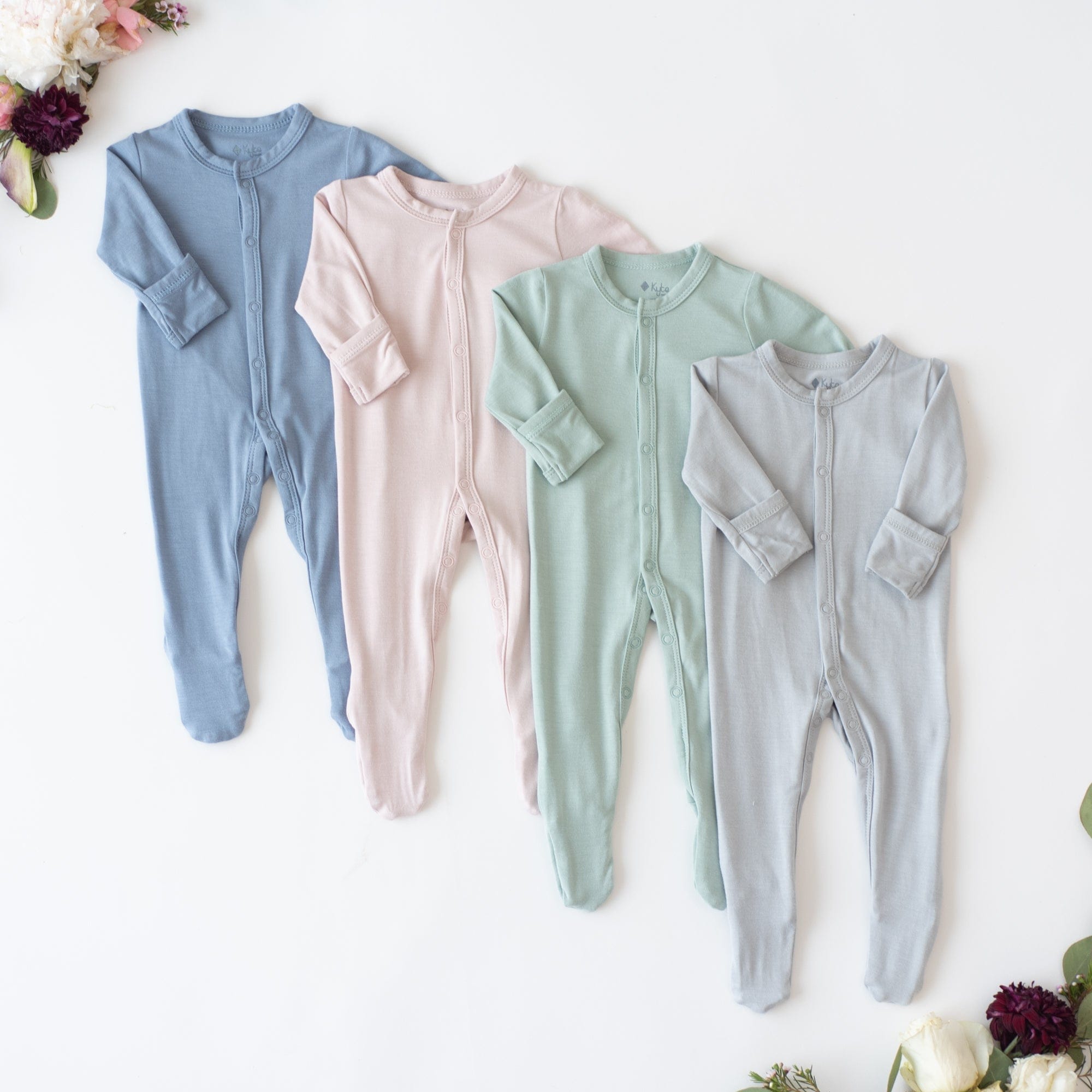 Flat lay of layered Kyte Baby Footies in Slate, Blush, Sage and Fog