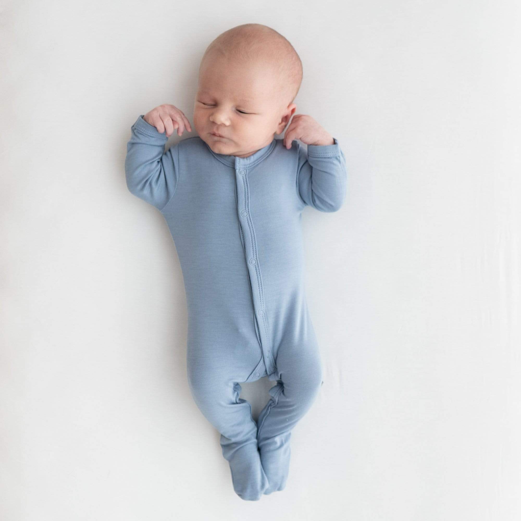 Sleeping newborn with arms up and wearing Kyte Baby Footie in Slate