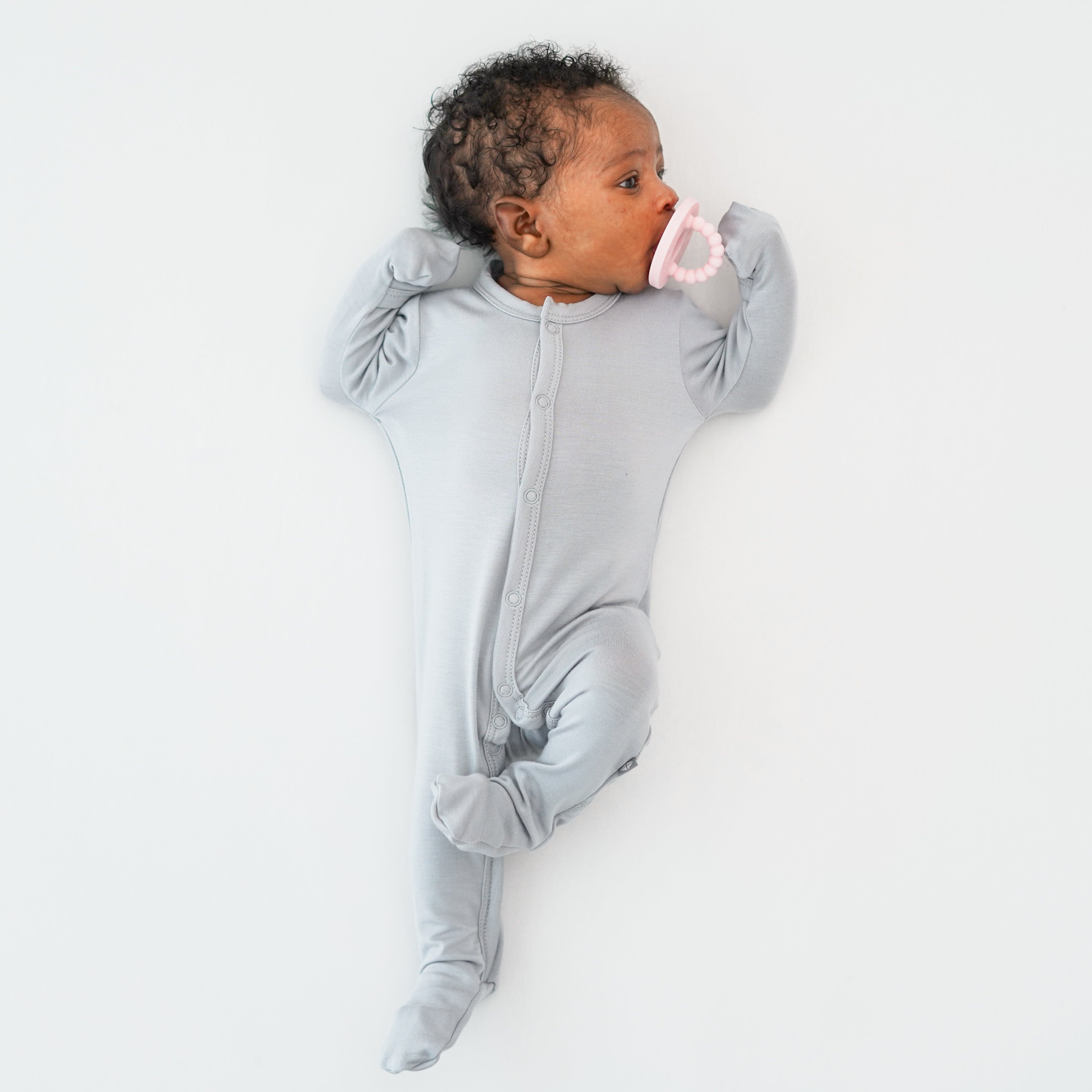 Newborn wearing Kyte Baby Footie in Storm with a pink pacifier