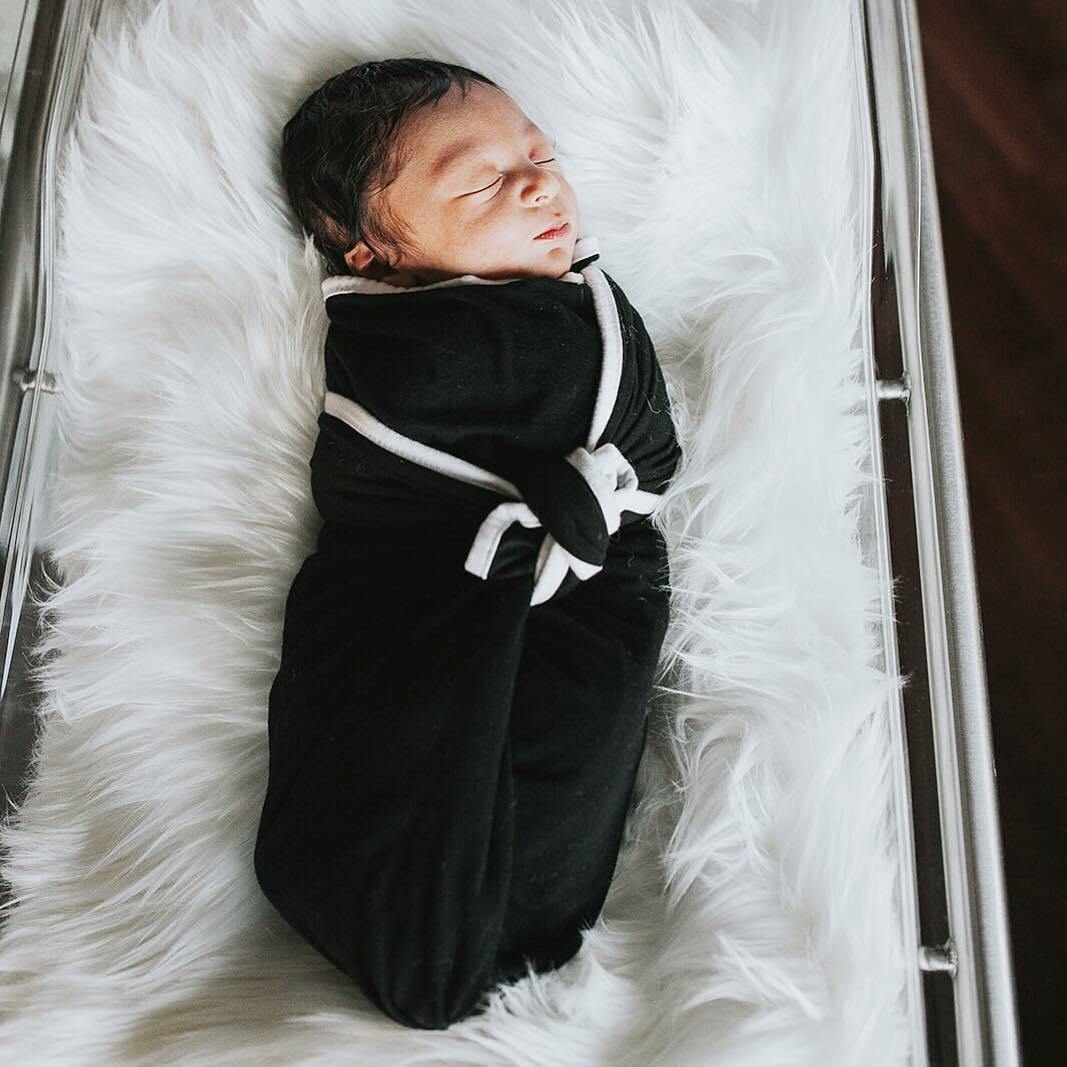 Newborn sleeping in Kyte Baby Swaddle Blanket in Midnight with Cloud Trim