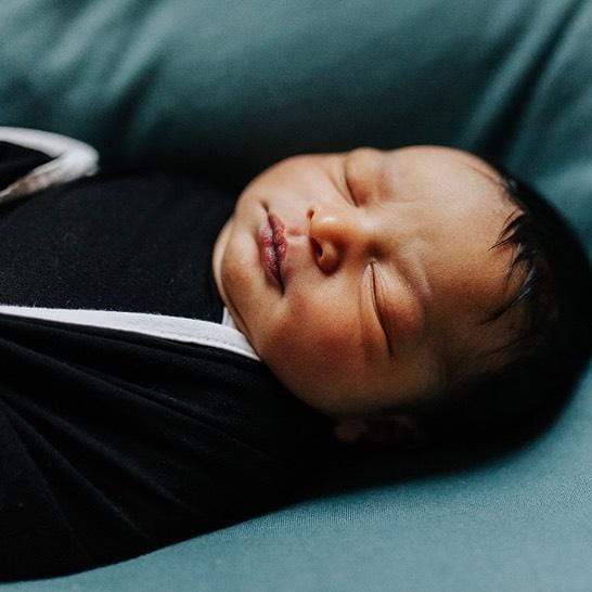 Newborn swaddled in Kyte Baby Swaddle Blanket in Midnight with Cloud Trim