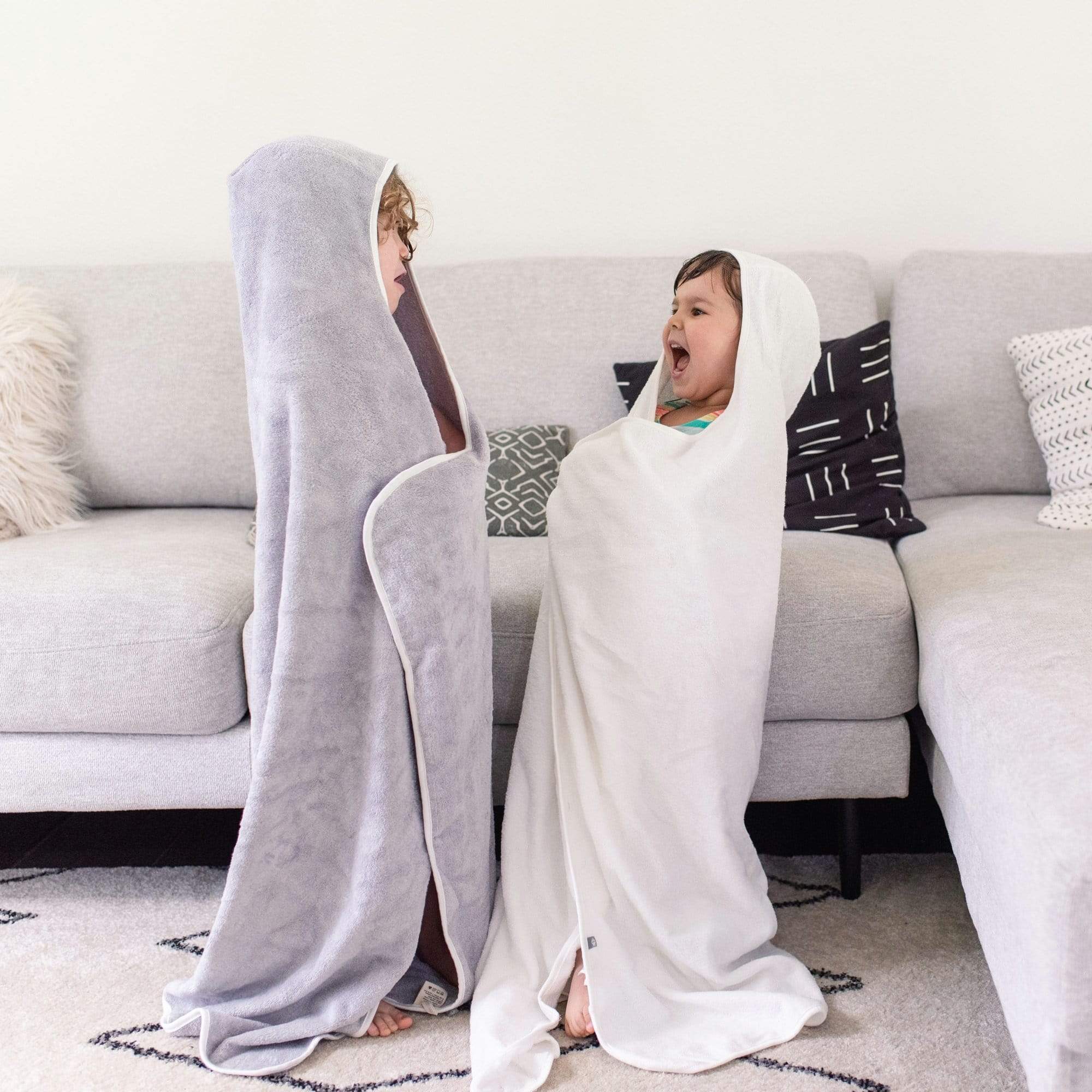 Two children in a living room wrapped in Kyte Baby Toddler Hooded Bath Towels with hoods on