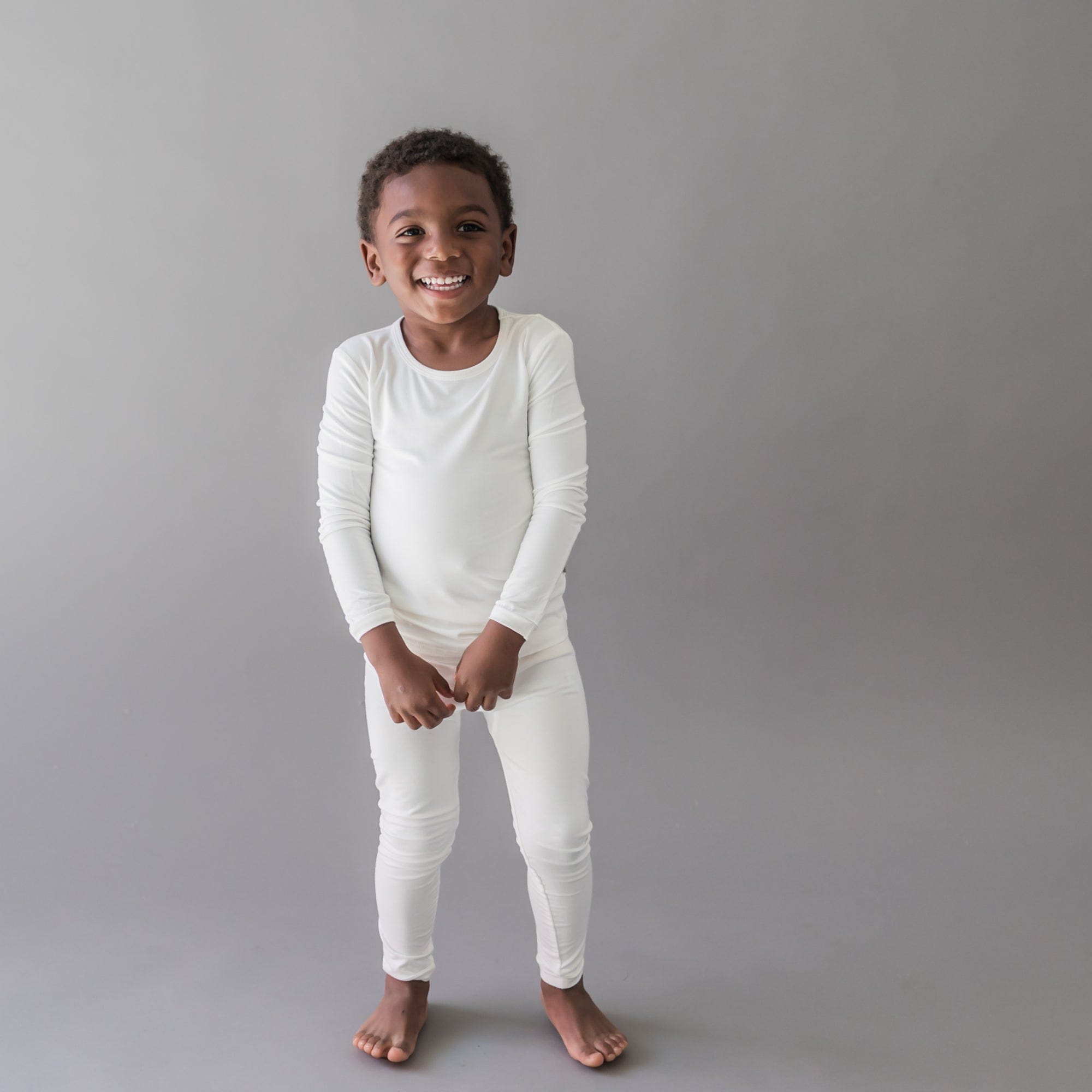 Smiling toddler wearing Kyte Baby Long Sleeve Pajama Set in Cloud