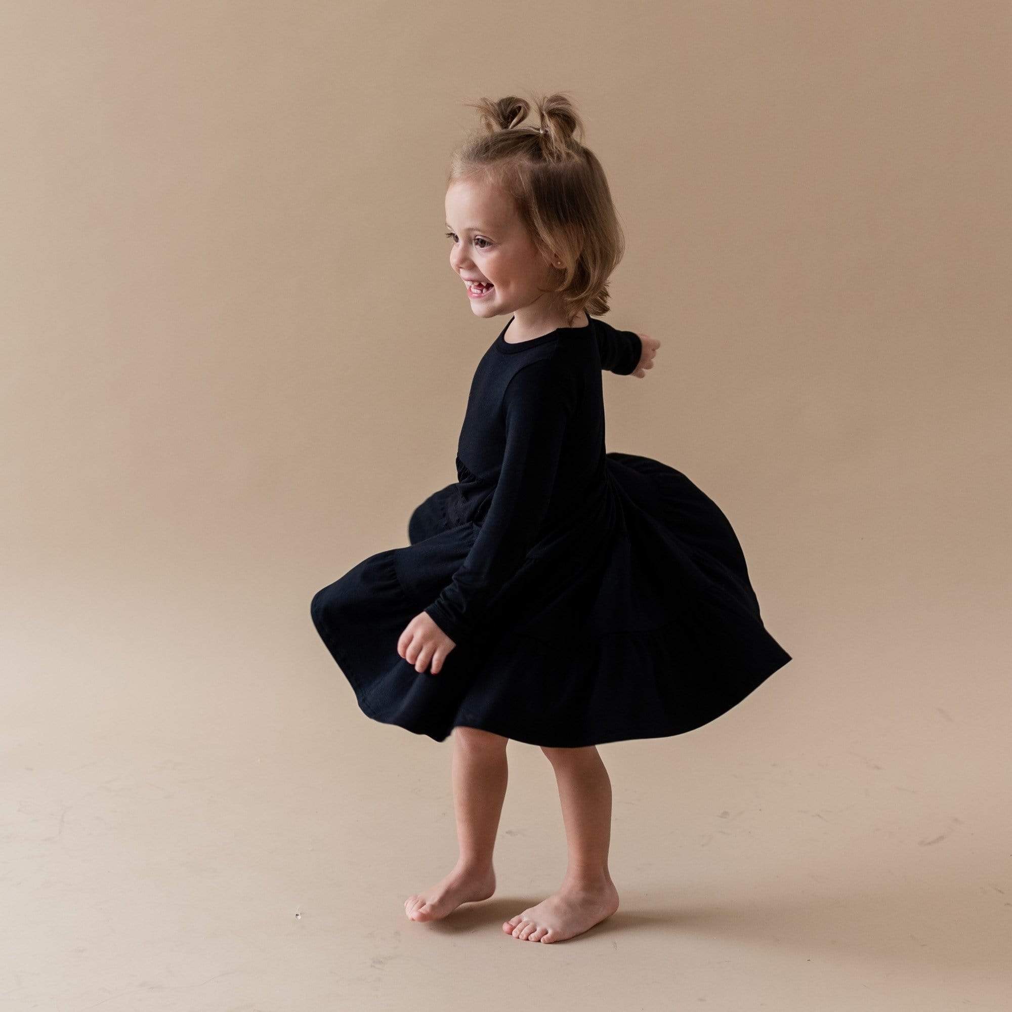 Toddler twirling in Kyte Baby Long Sleeve Tiered Dress in Midnight black