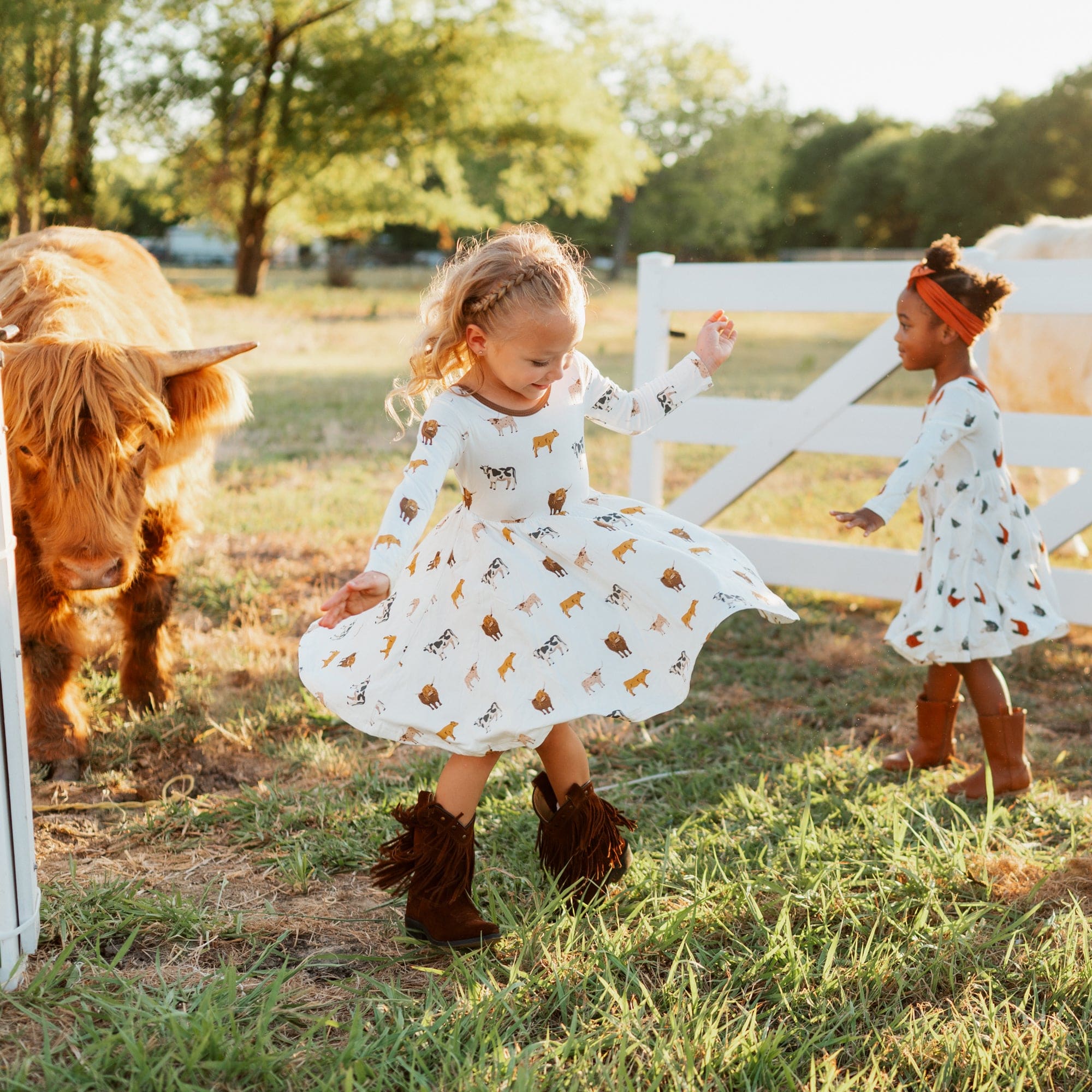 Girls wearing Kyte Baby Long Sleeve Twirl Dresses in Moo print with cow